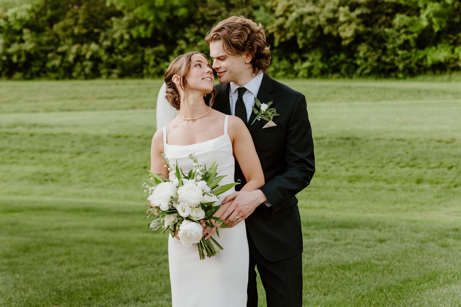 An elegant wedding portrait showing a tender embrace on a manicured lawn.