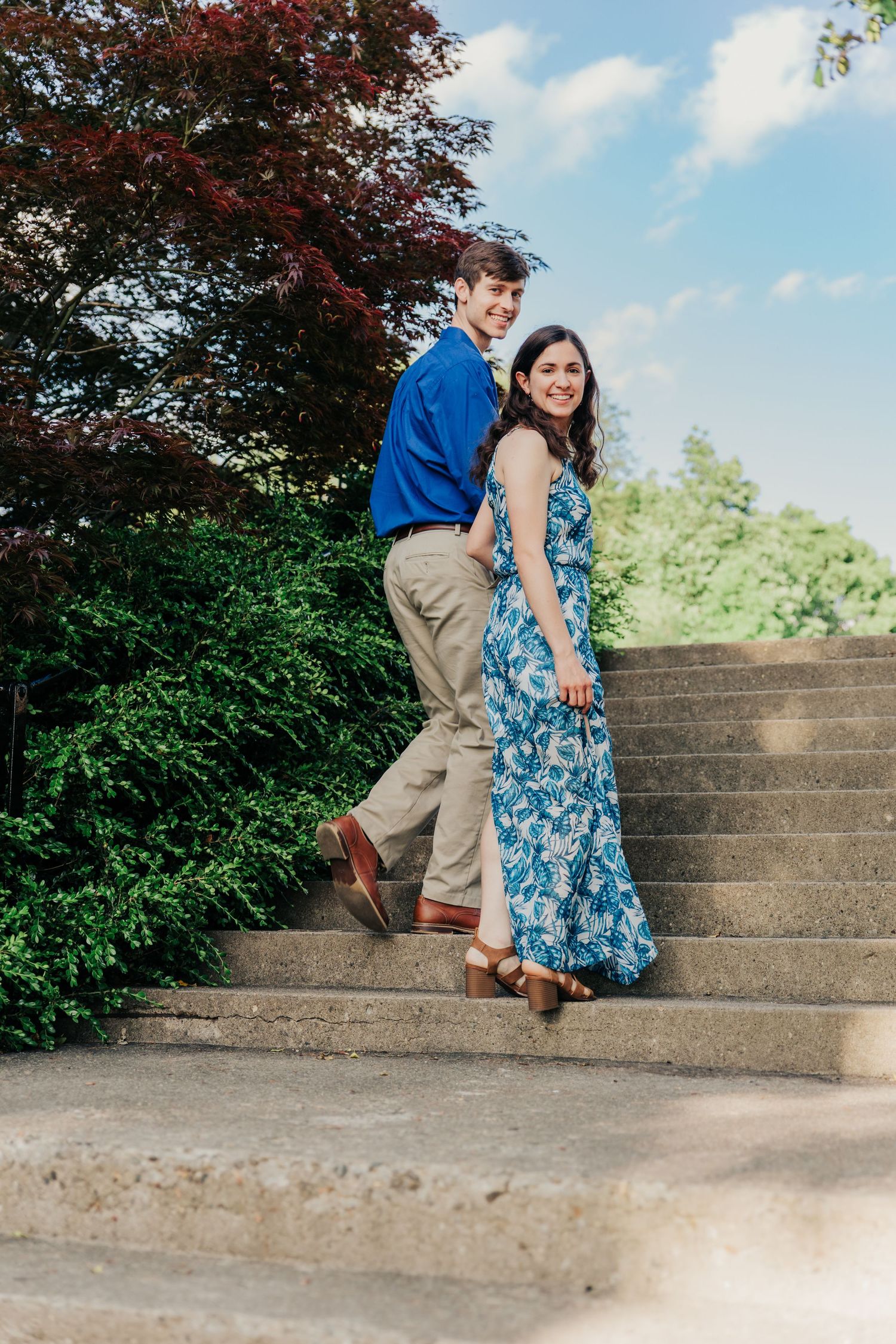 A couple playfully poses on stone steps in a garden setting.