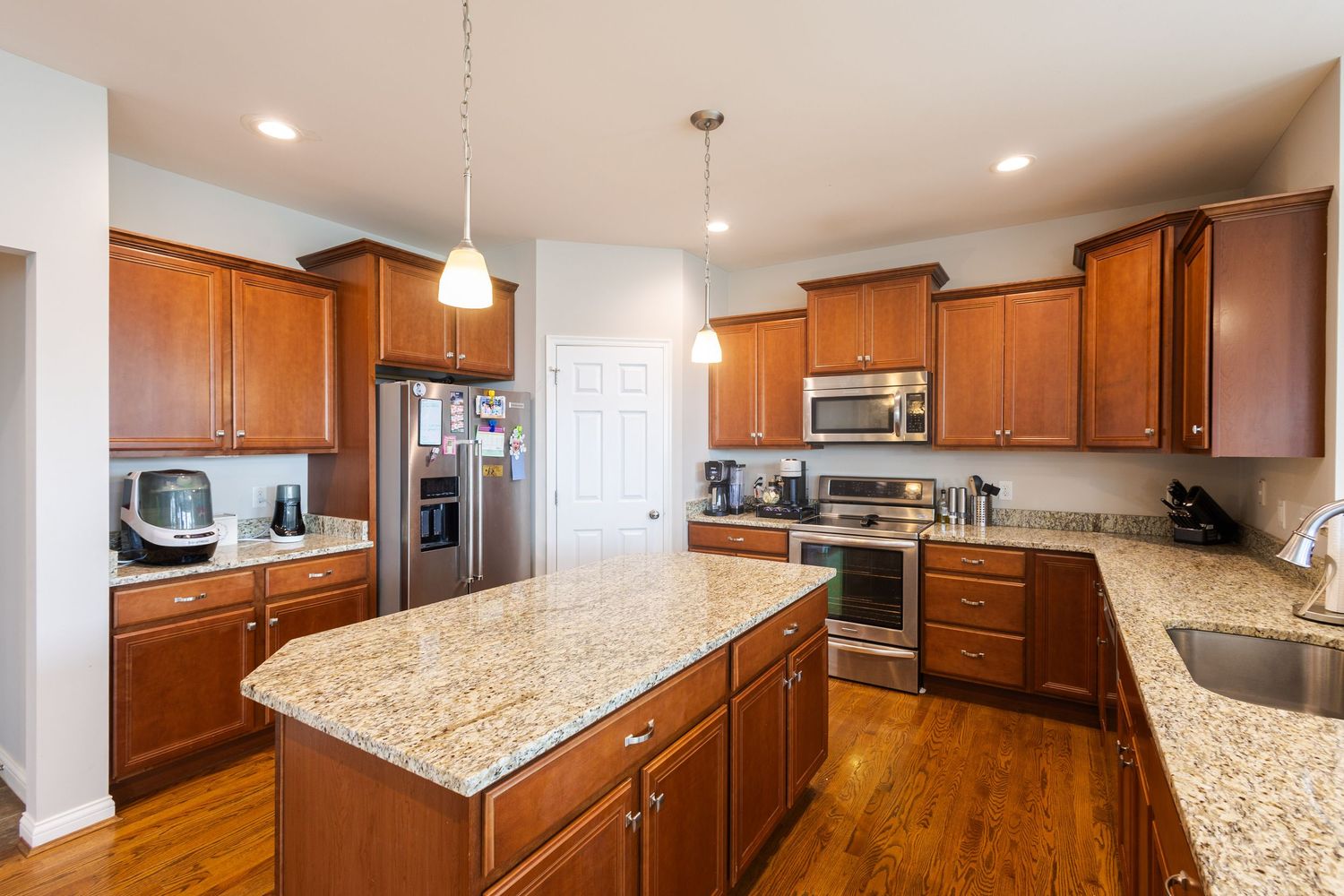 Spacious kitchen with cherry wood cabinets, granite island, stainless steel appliances, and hardwood floors.