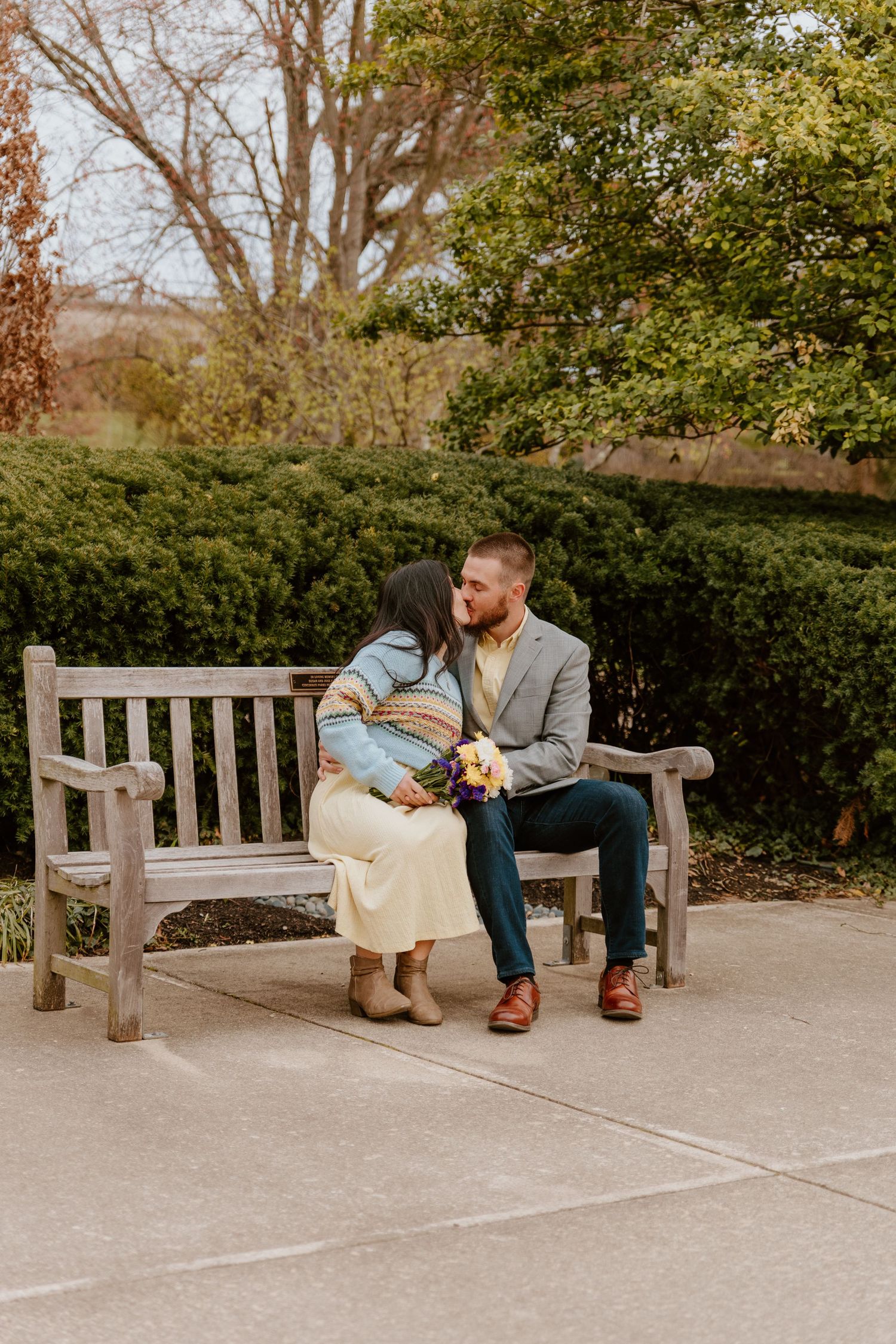 Couple sitting together on park bench surrounded by greenery.