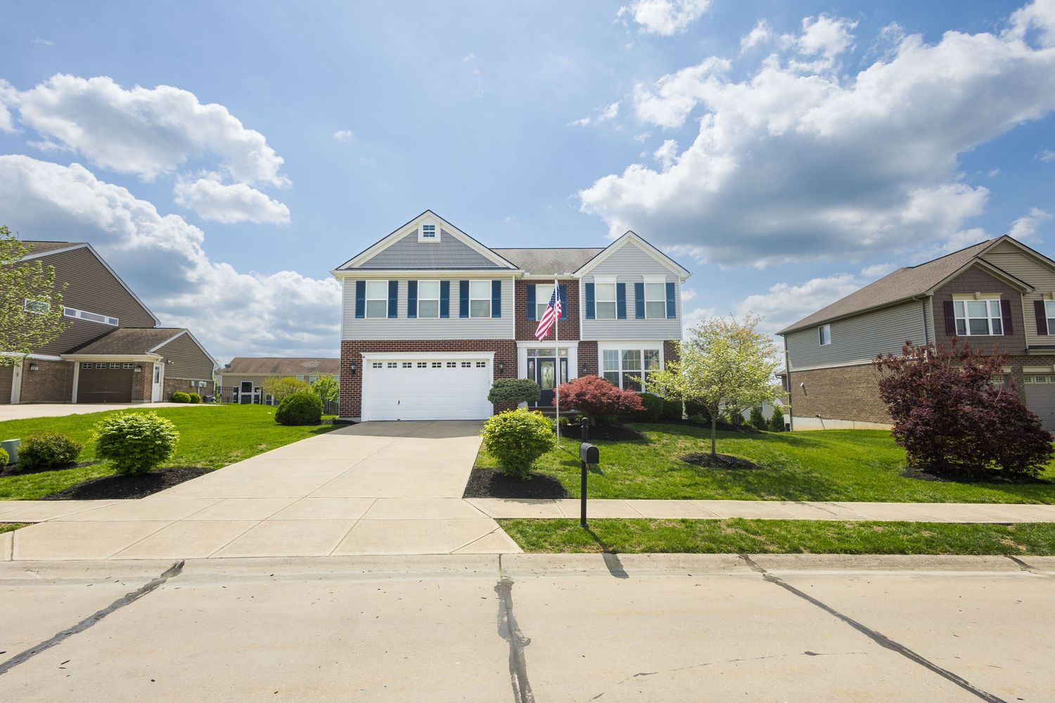 Two-story suburban home with white siding, green shutters, two-car garage, and lush lawn under a partly cloudy sky.