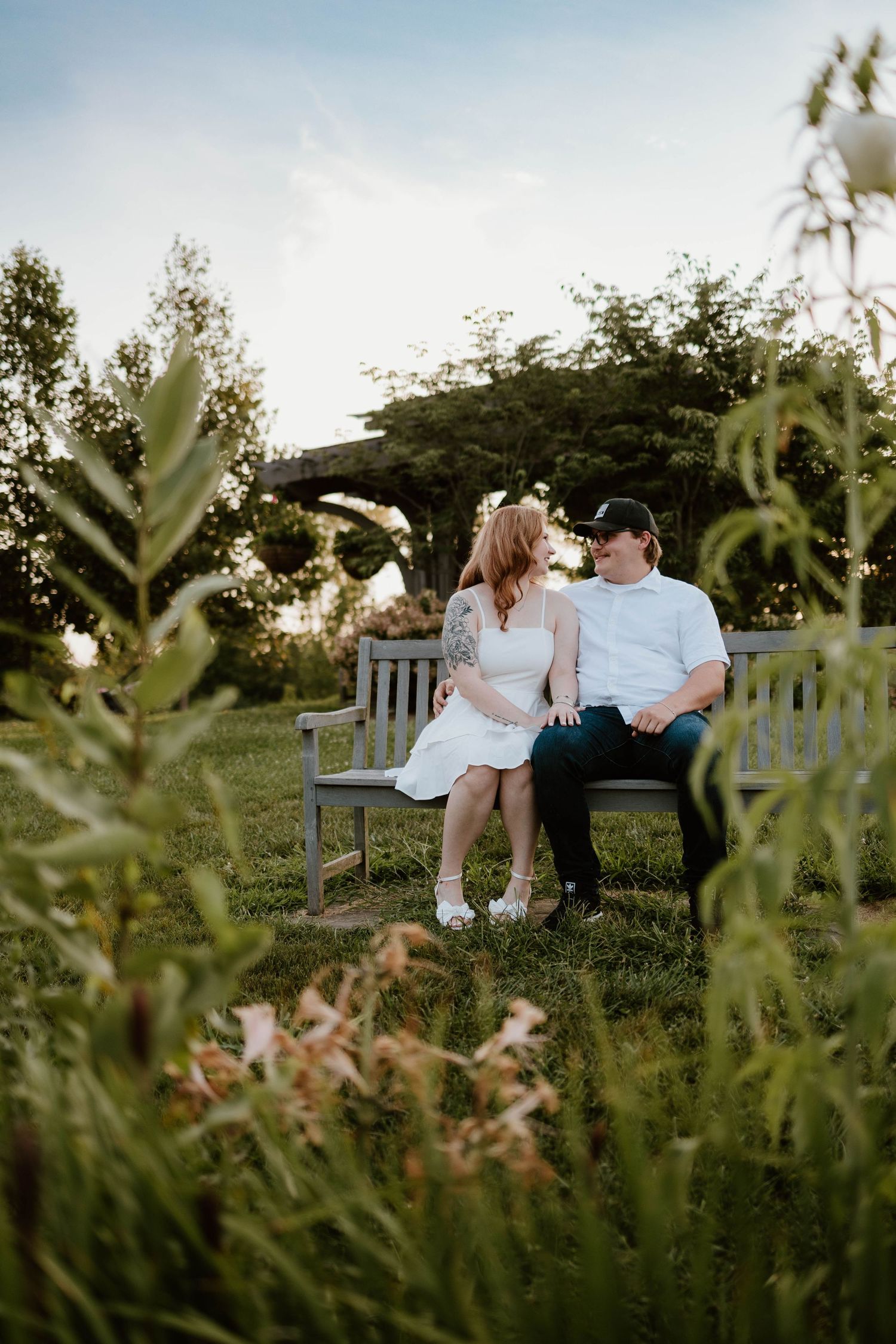 Couple sitting together on a wooden bench in a lush garden setting at golden hour.