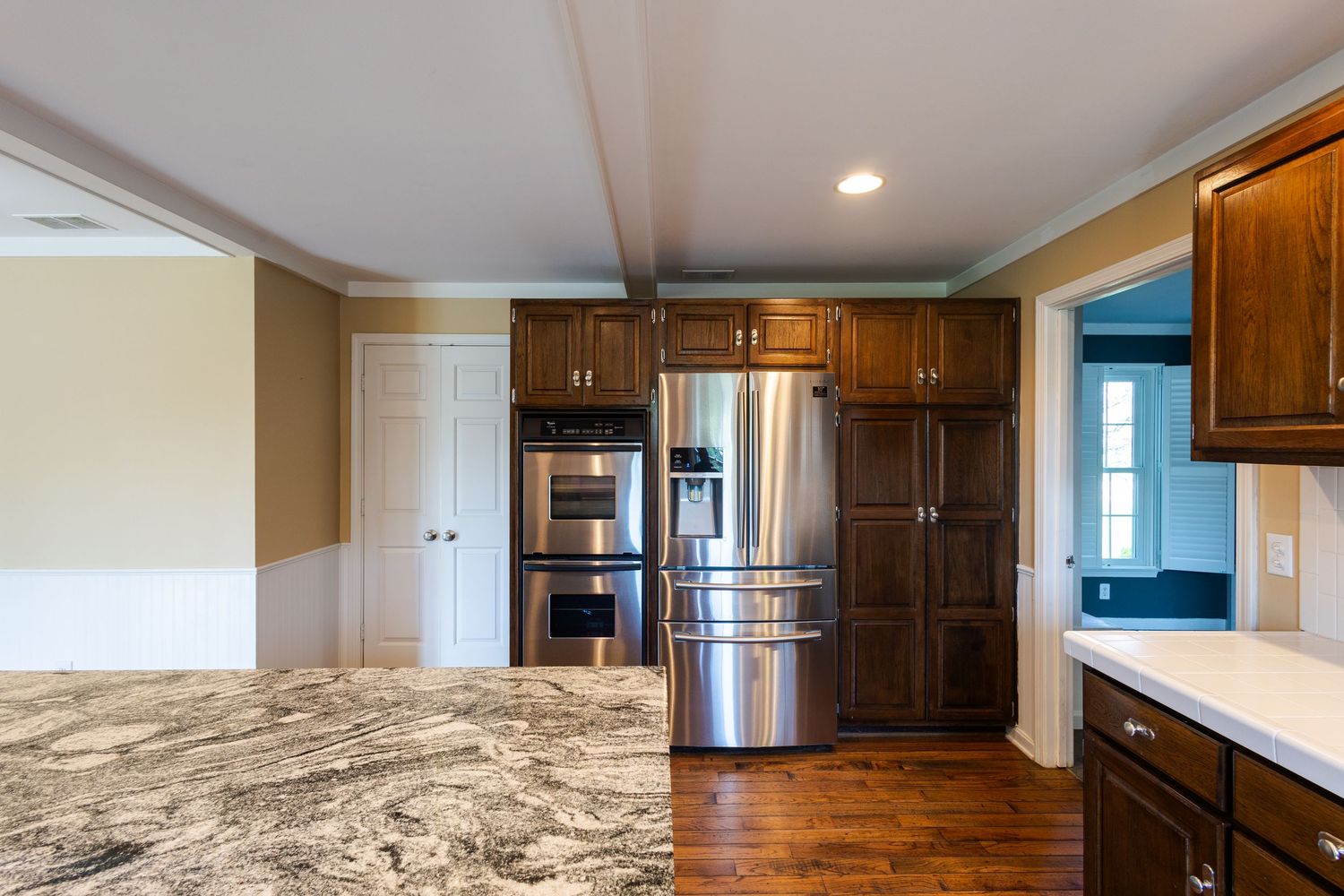 Modern kitchen with dark wood cabinets, stainless steel appliances, granite countertops, and hardwood floors.