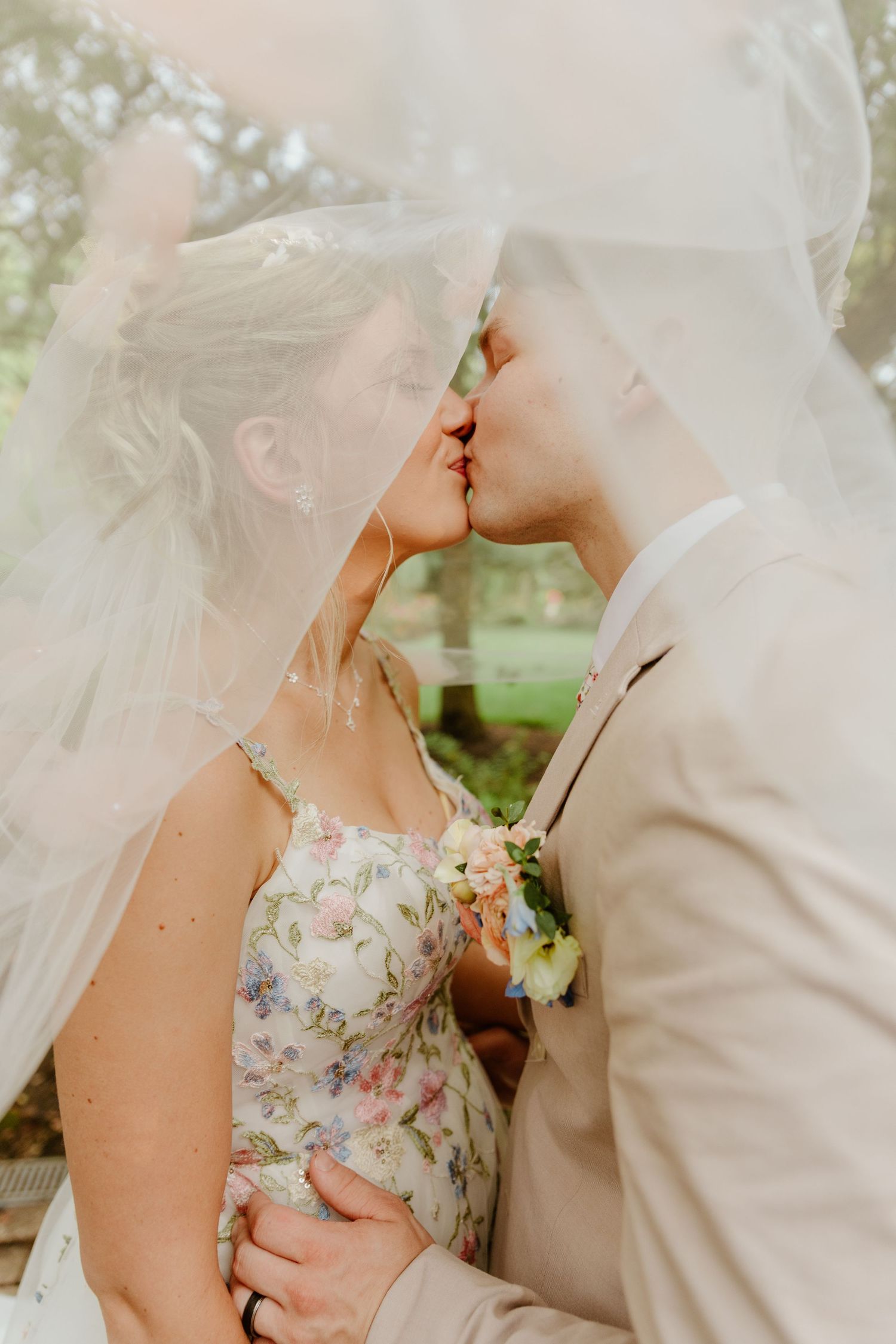 A romantic wedding couple shares an intimate moment under a flowing white veil in an outdoor garden setting.
