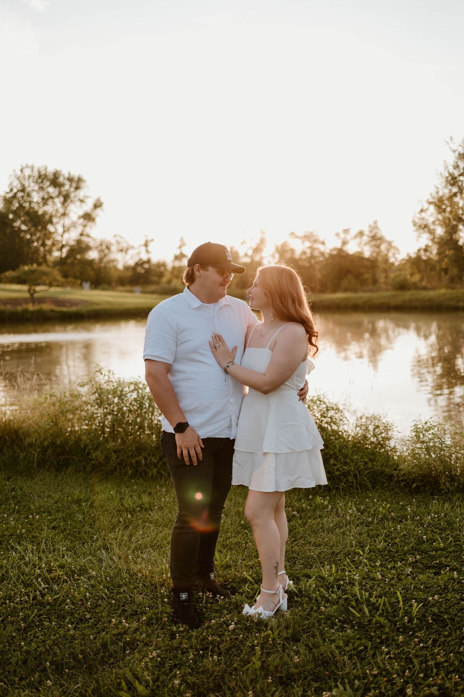 Romantic lakeside portrait at golden hour with matching white outfits.