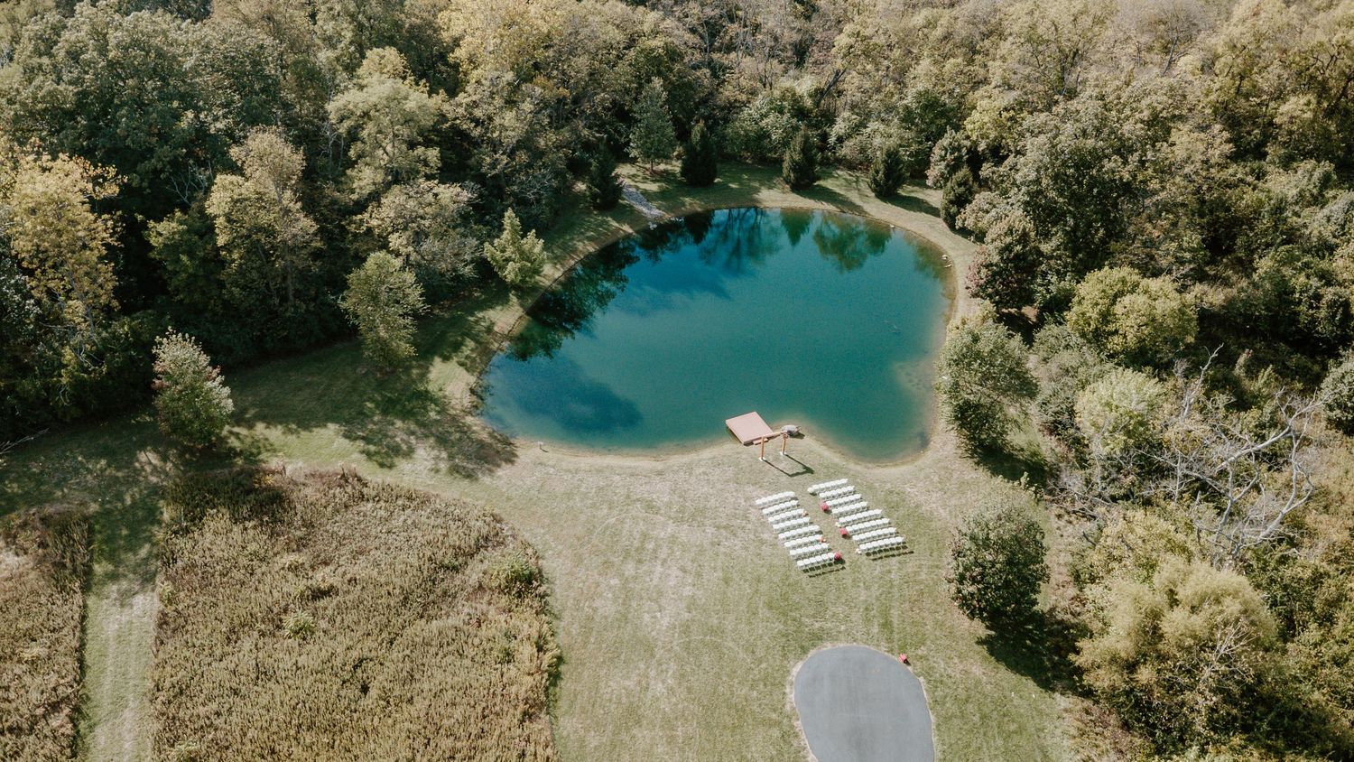 Aerial panoramic view of a turquoise lake surrounded by lush forest and beach chairs on a sunny day.
