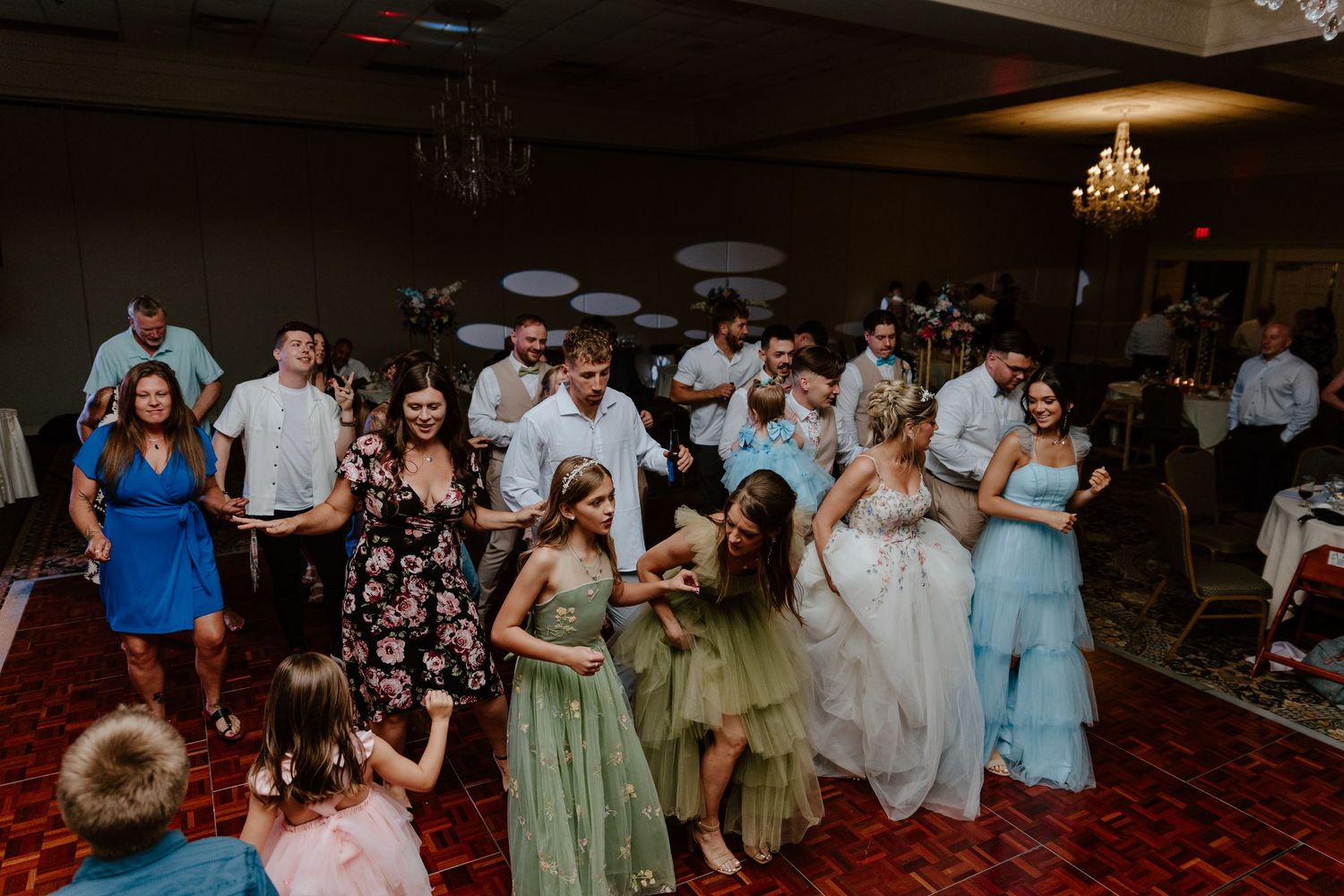 Wedding guests dance together on the dance floor during an evening reception celebration.