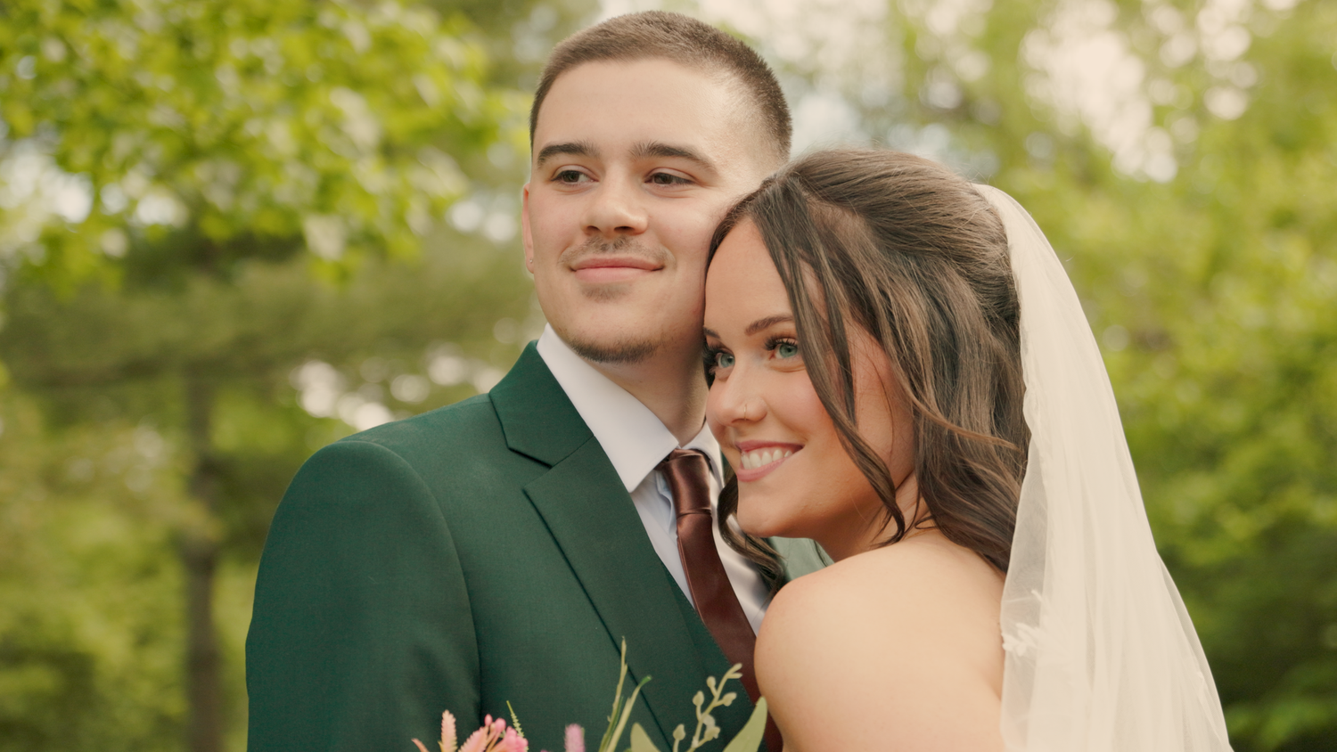 An intimate wedding portrait captured outdoors with natural lighting and green foliage.