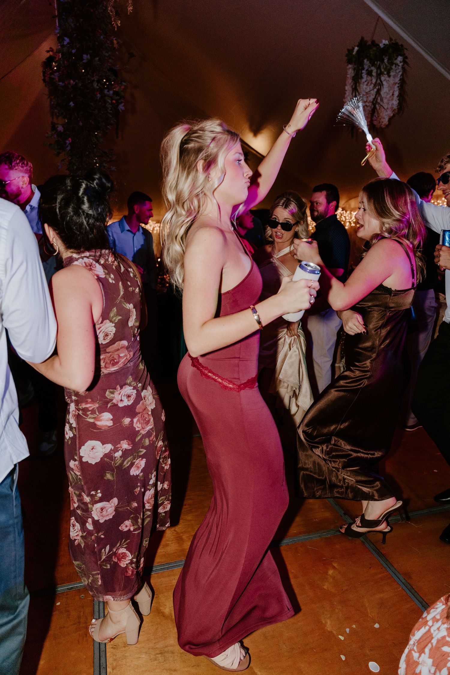 People dancing and having fun at a party with burgundy and floral dresses on a wooden dance floor.