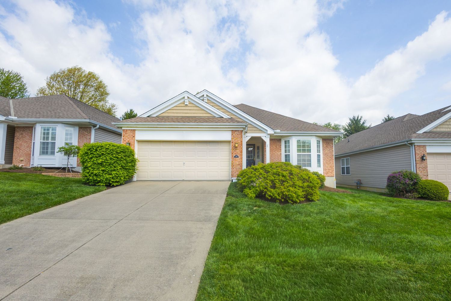 Single-story brick ranch home with attached two-car garage, lush green lawn, and manicured shrubs on a sunny day.