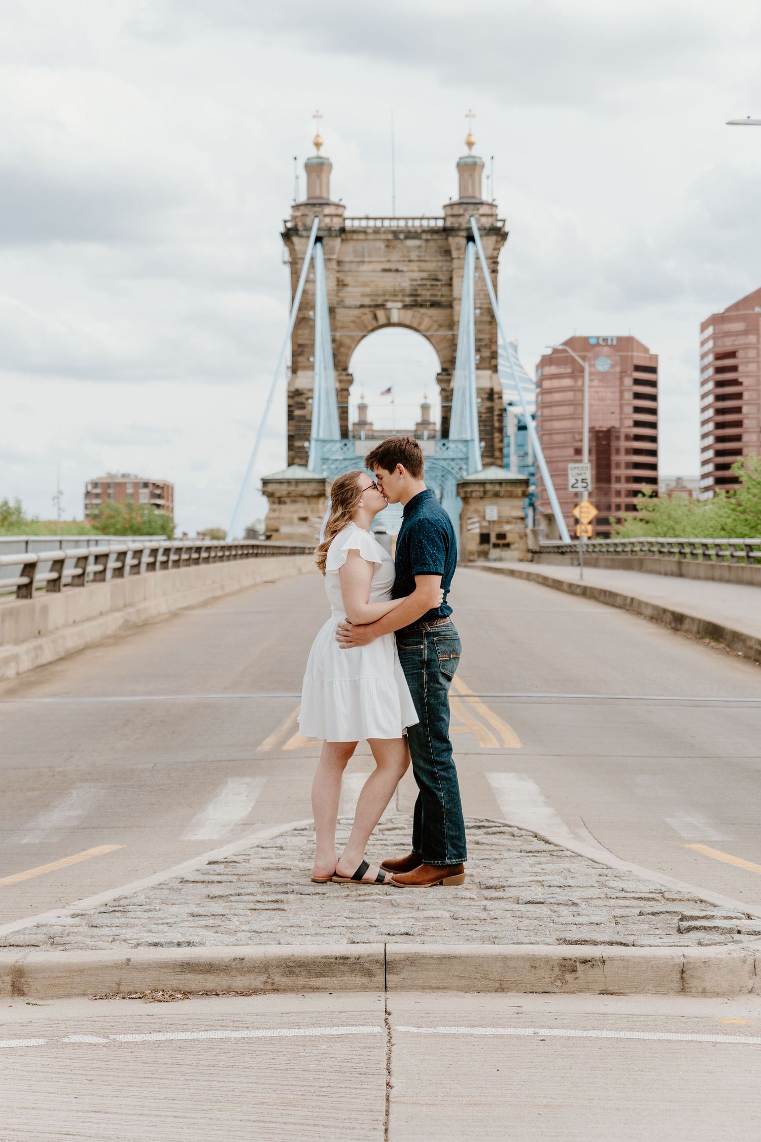 Romantic couple shares tender moments on historic stone bridge with city buildings in background.