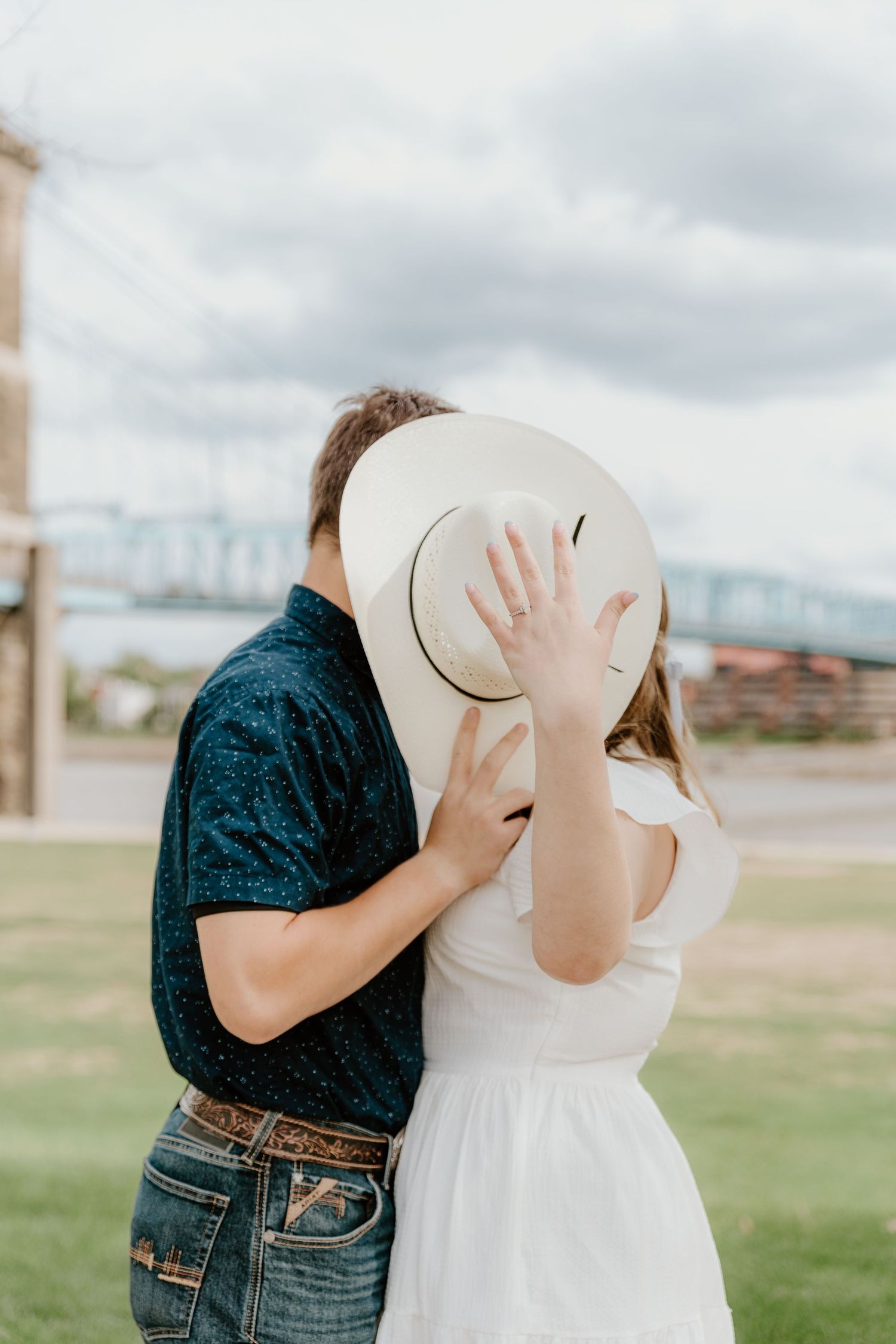 Romantic couple embracing while wearing cowboy hats against cloudy sky.