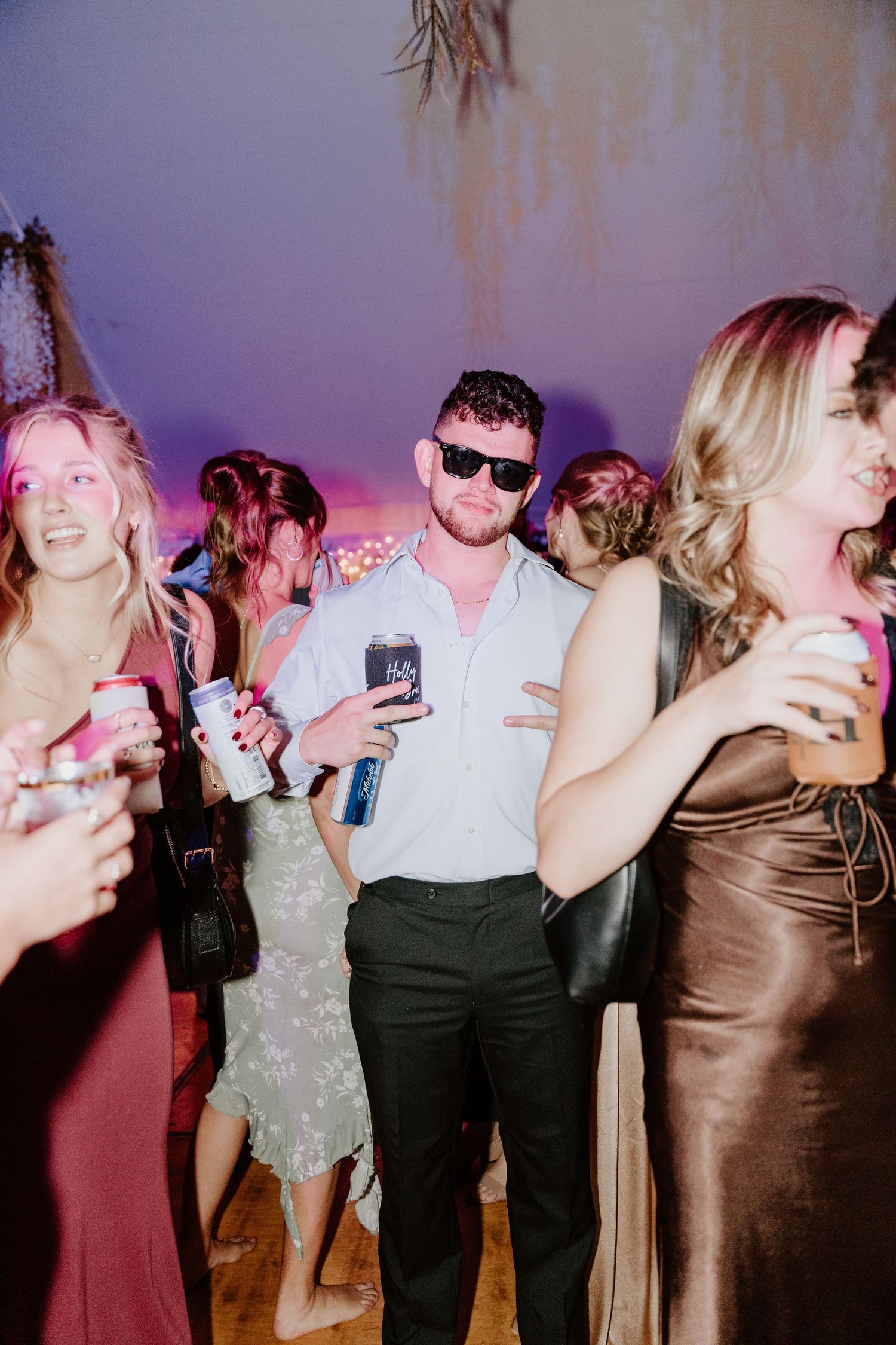 A group of party guests dancing and celebrating at a festive event with colorful purple lighting in the background.
