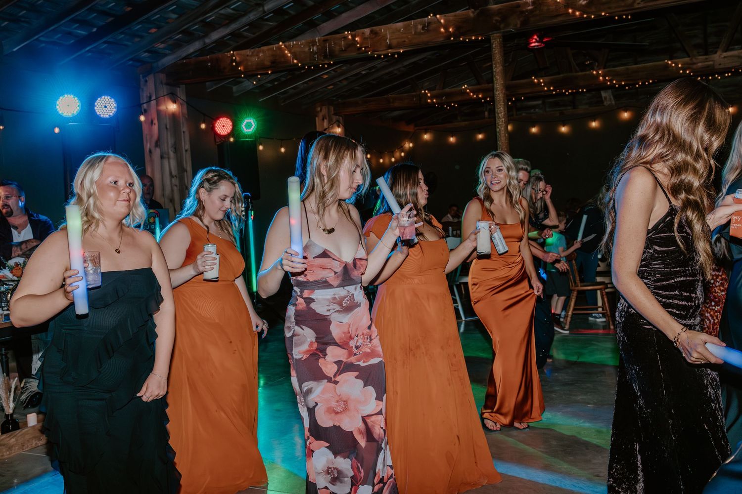 A group of people dancing and enjoying themselves at a party with colorful lights and a rustic venue setting.