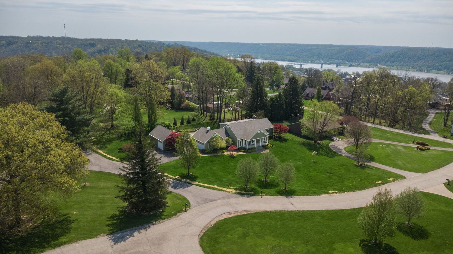 Aerial view of a luxury home surrounded by lush green trees near a scenic lake in a peaceful neighborhood.