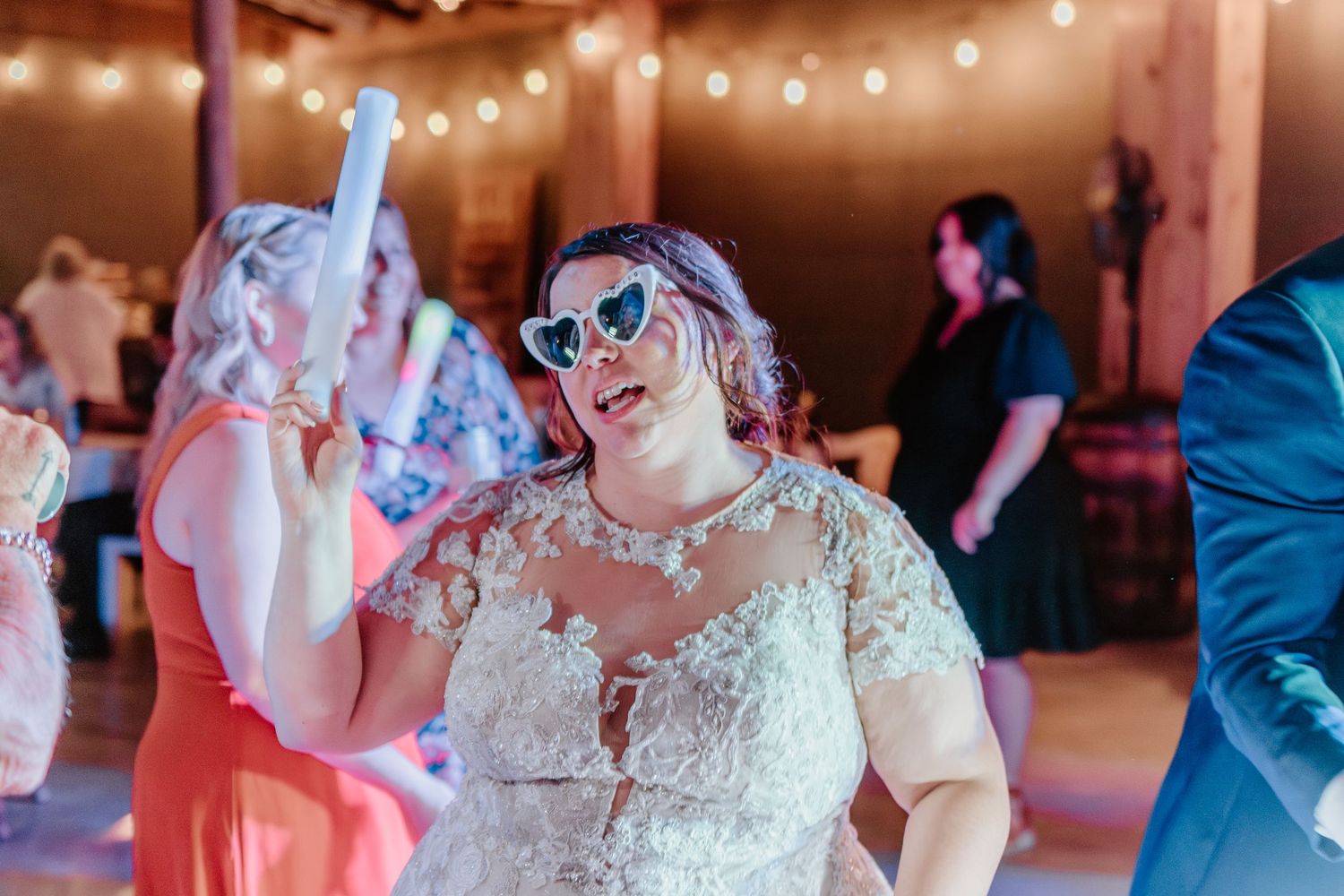 Wedding guests dance and celebrate on a dimly lit dance floor decorated with string lights overhead.