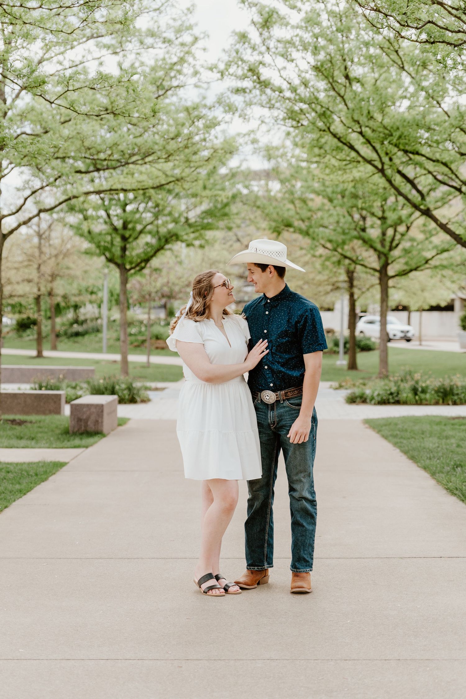 Couple walking together on tree-lined pathway during spring engagement photo session.