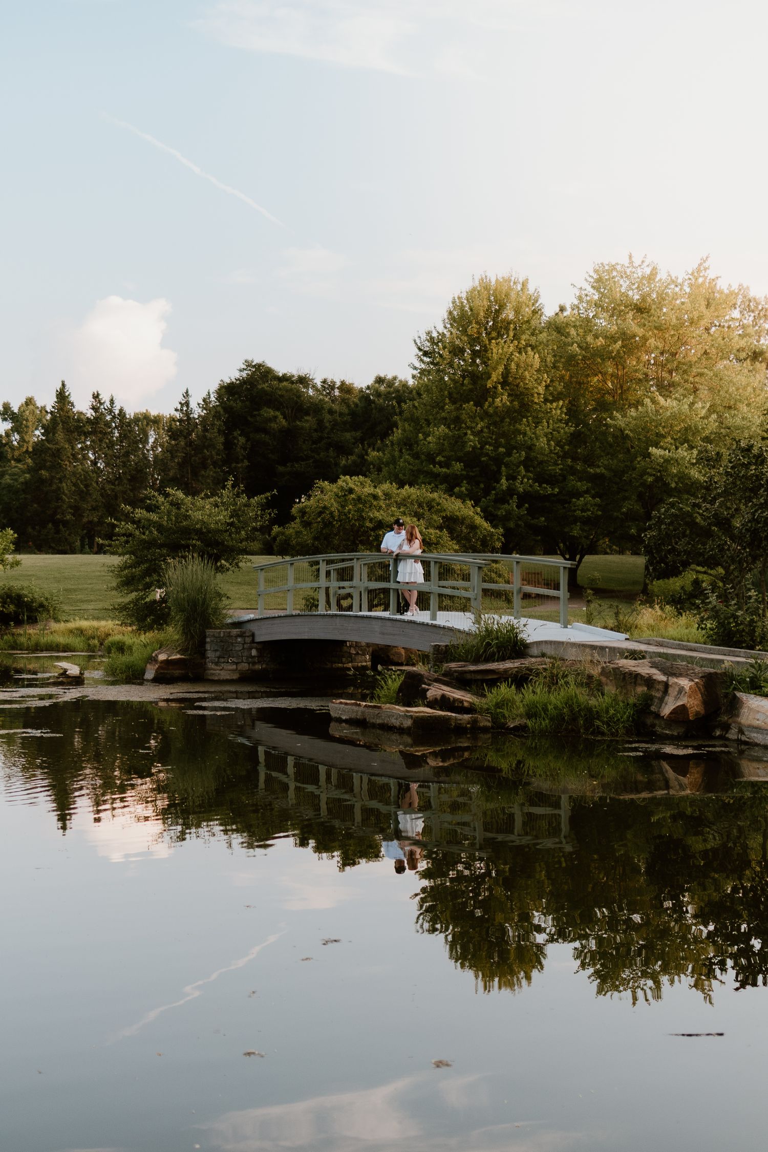 Serene lakeside landscape with wooden bridge and trees reflecting in calm water during golden hour.