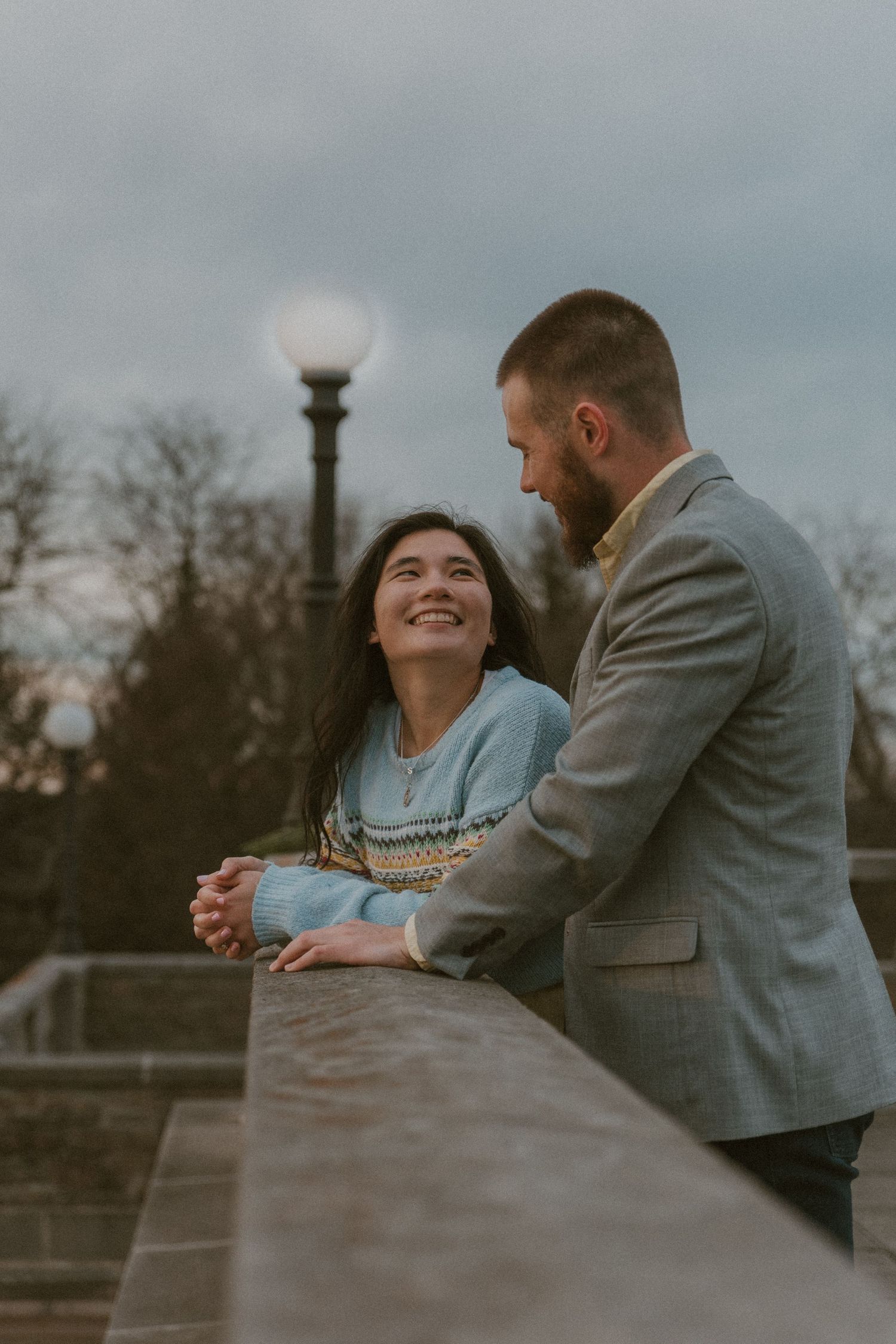 A couple shares a tender moment while leaning against a concrete railing at sunset.