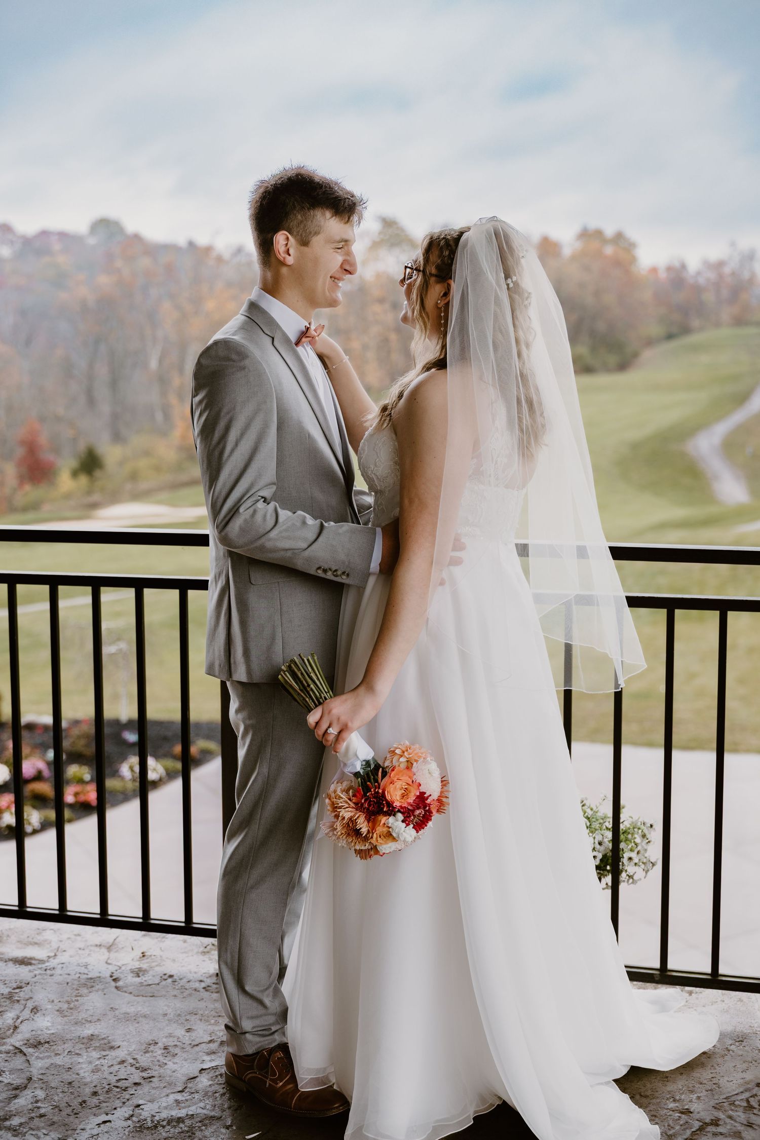 Newlywed couple shares romantic moments on a balcony overlooking an autumn landscape in elegant wedding attire.