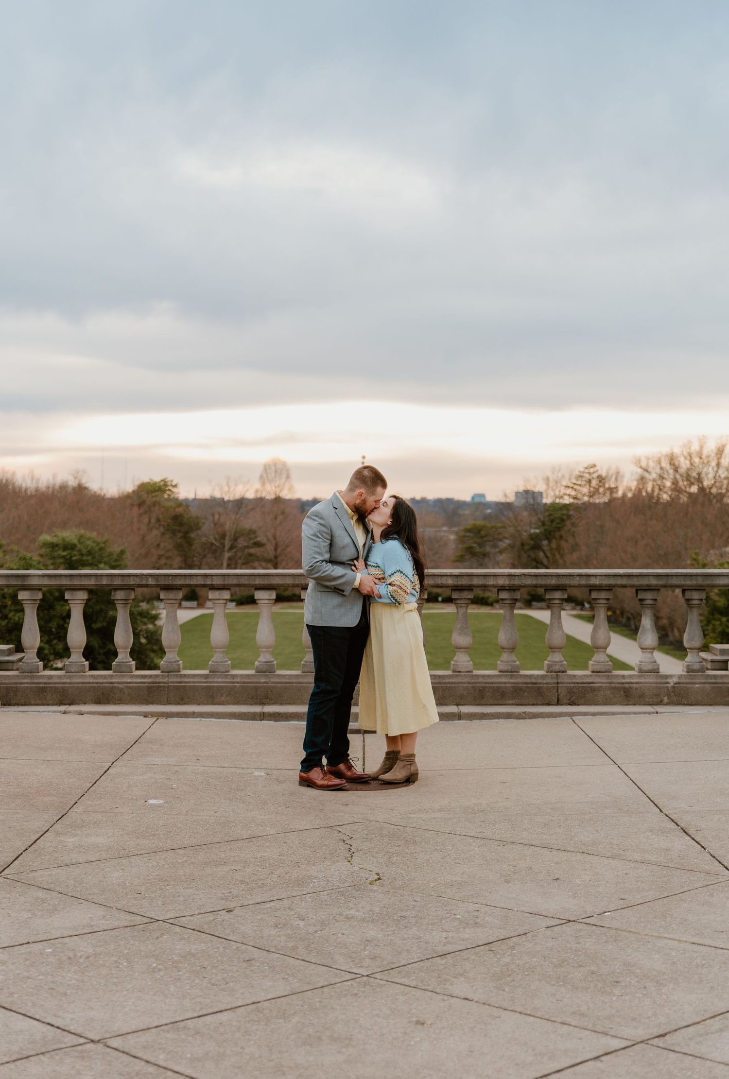 A romantic proposal scene unfolds on a stone terrace overlooking a scenic landscape.