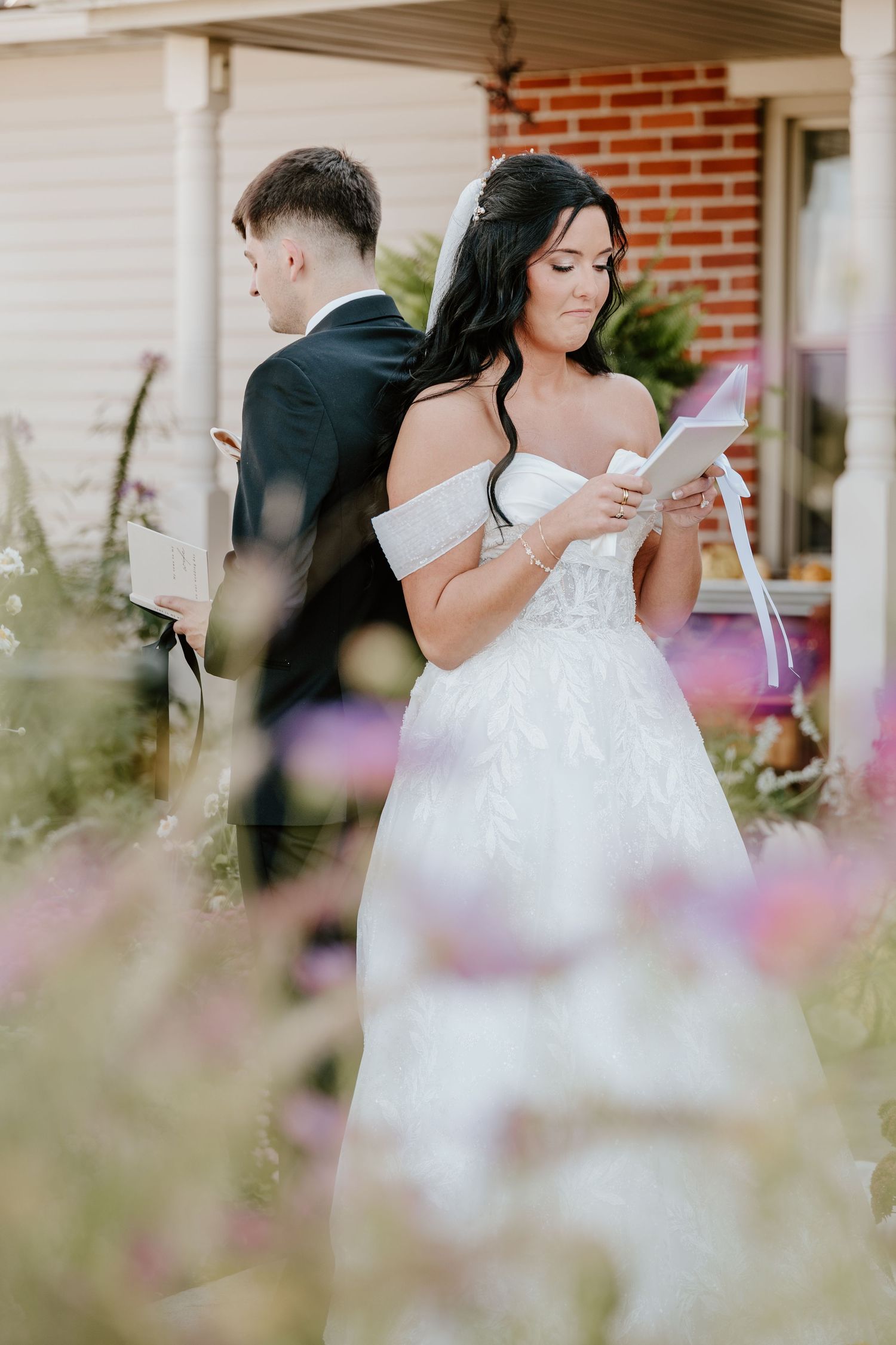A couple reading letters back-to-back during their first look moment at an outdoor wedding ceremony.