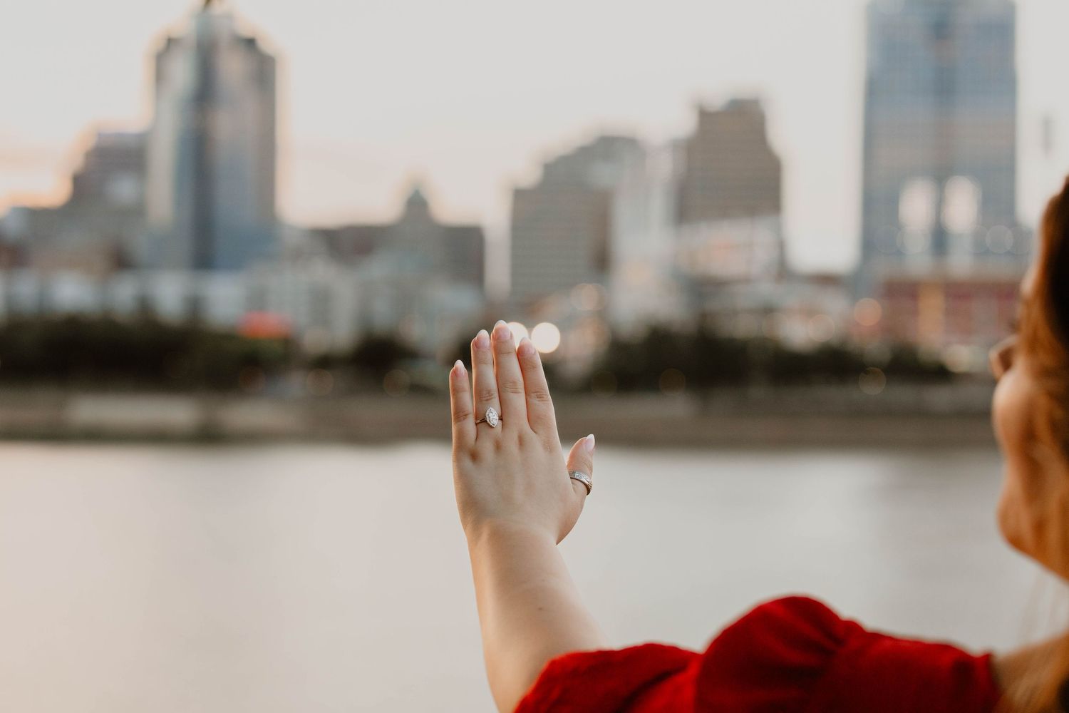 Woman in red dress raising arms joyfully against city skyline backdrop.