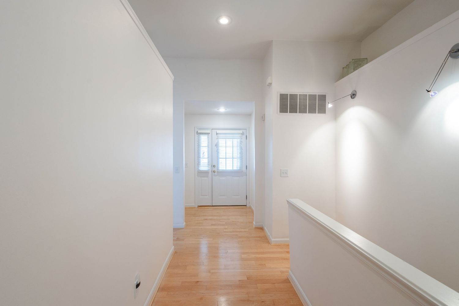 Bright hallway with white walls, hardwood floors, recessed lighting, and a white door with window at the end.