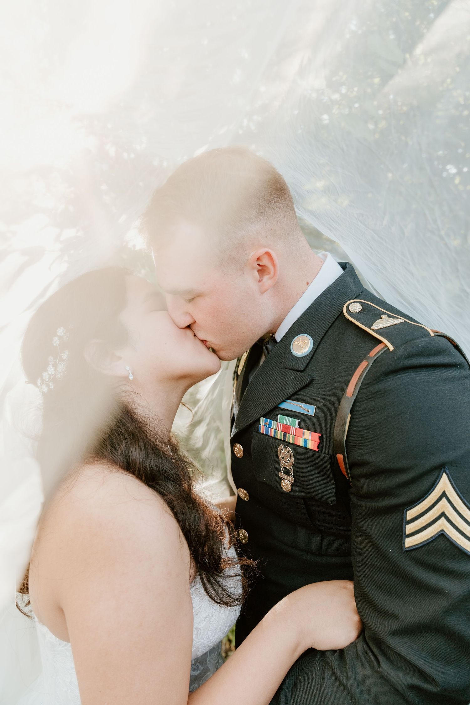 Military groom in dress uniform kissing bride under veil on wedding day.