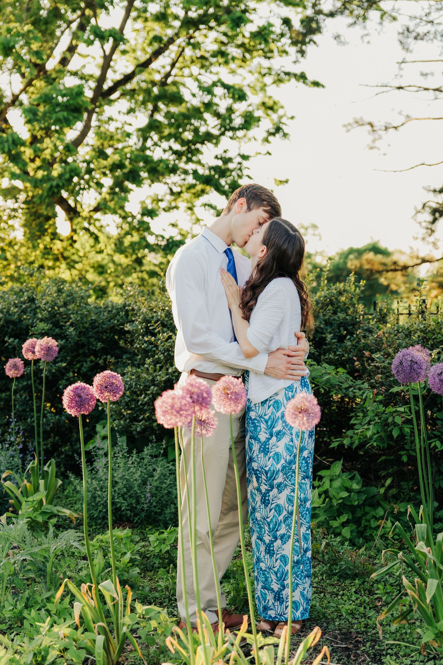 A couple shares an intimate moment among blooming pink flowers in a garden.