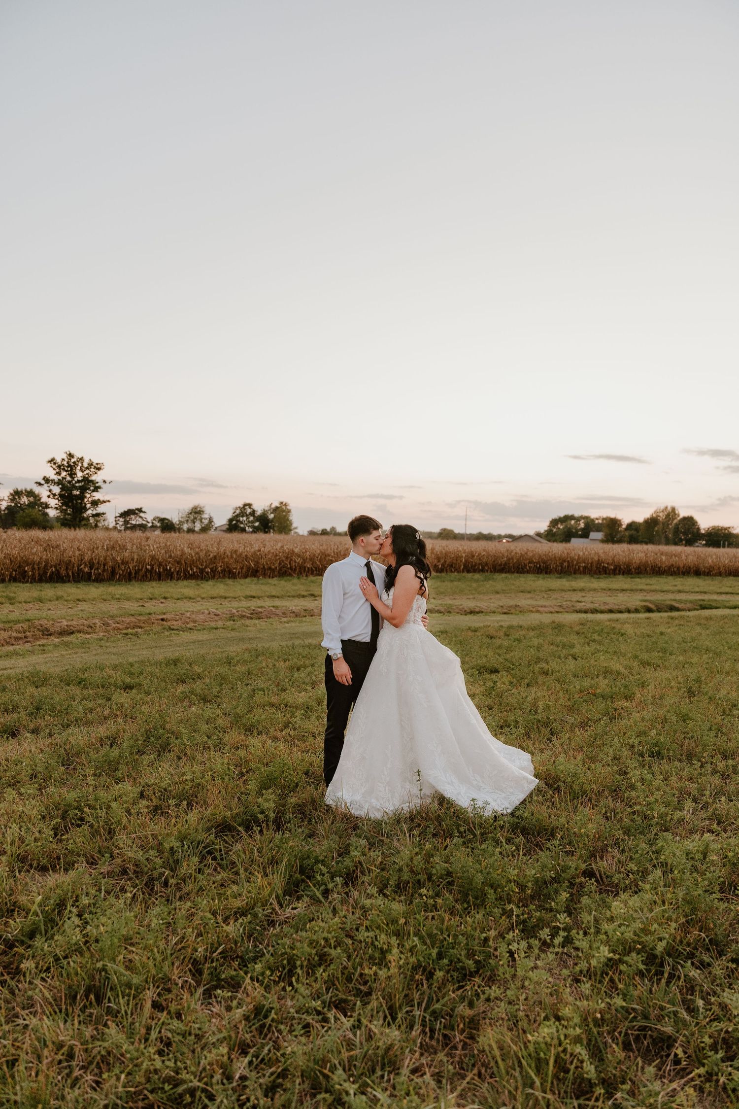 Sunset wedding portraits in a rustic field with cornfields and open sky in the background.