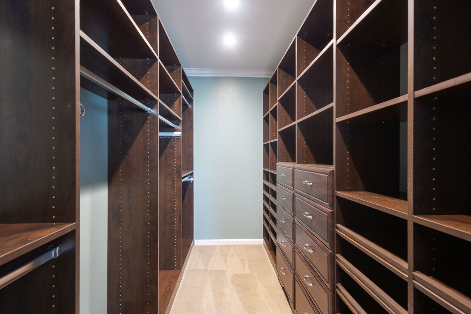 Spacious walk-in closet with dark wood shelving units, hanging rods, and light hardwood floors in a luxury home.