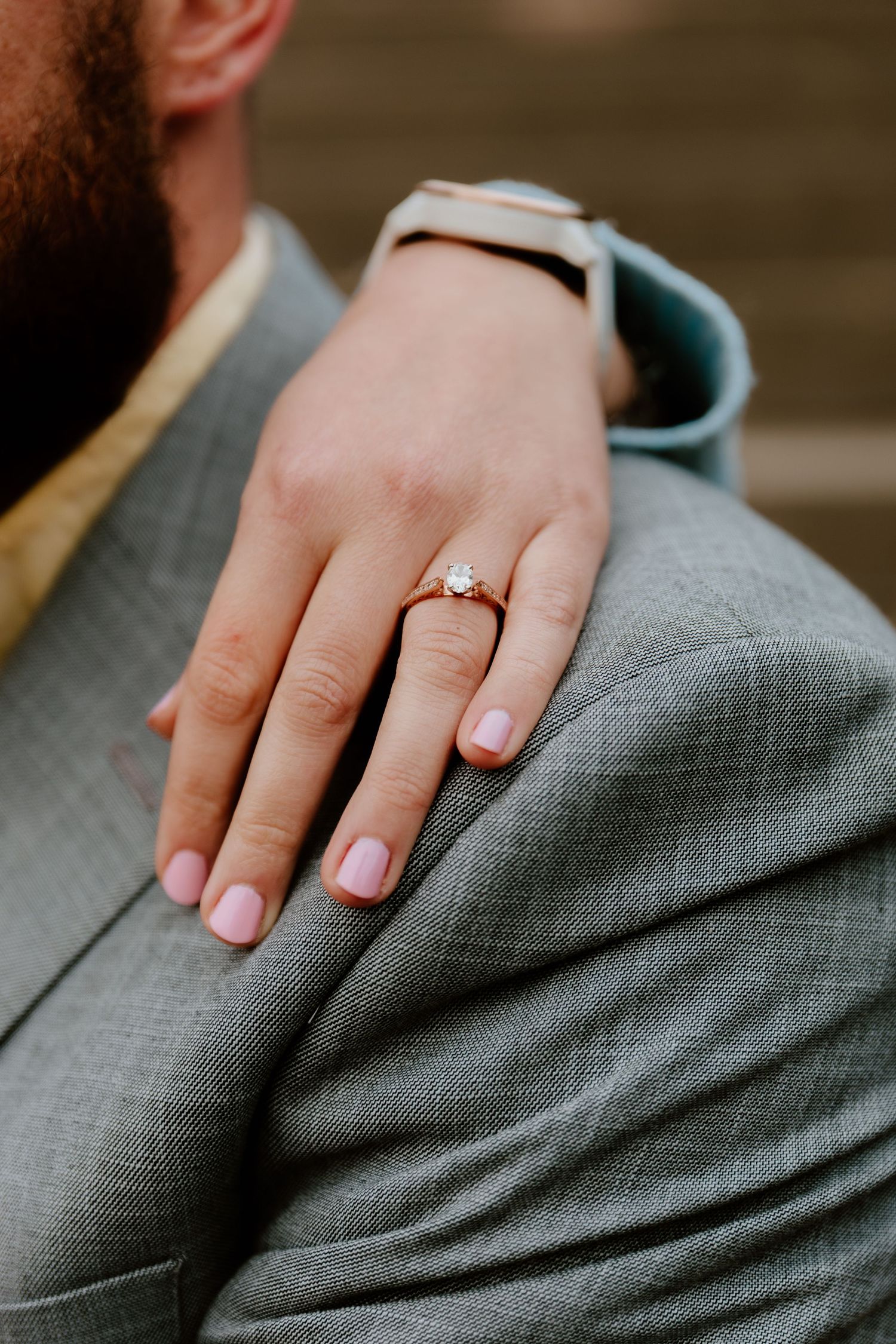 Close-up of engagement ring on hand resting against grey fabric.