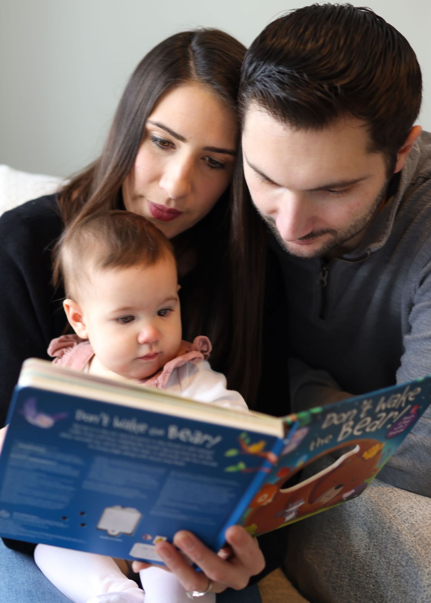Family reads a children's picture book together while sitting close on a couch.