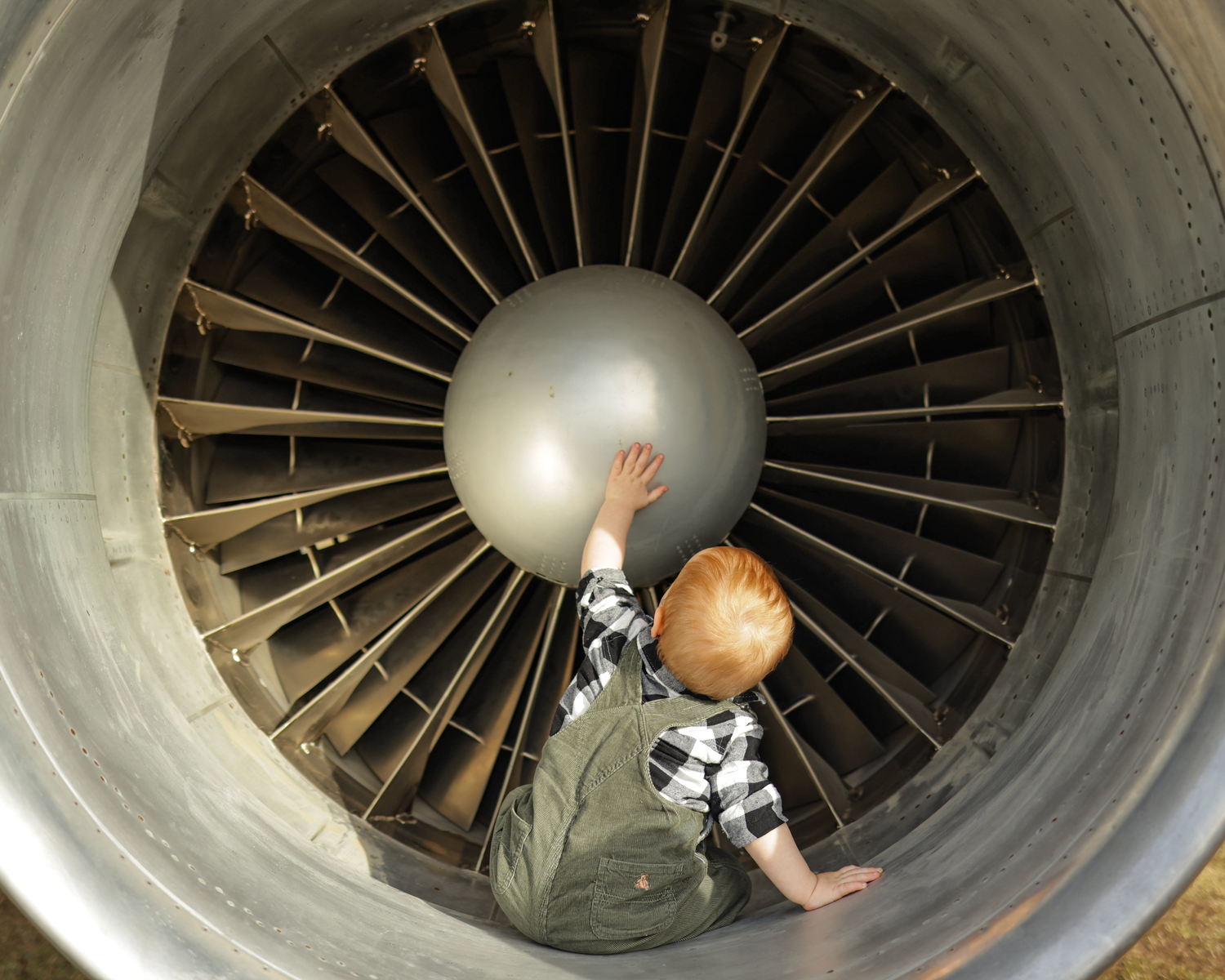Young child exploring inside a large jet engine turbine at an aviation museum display.