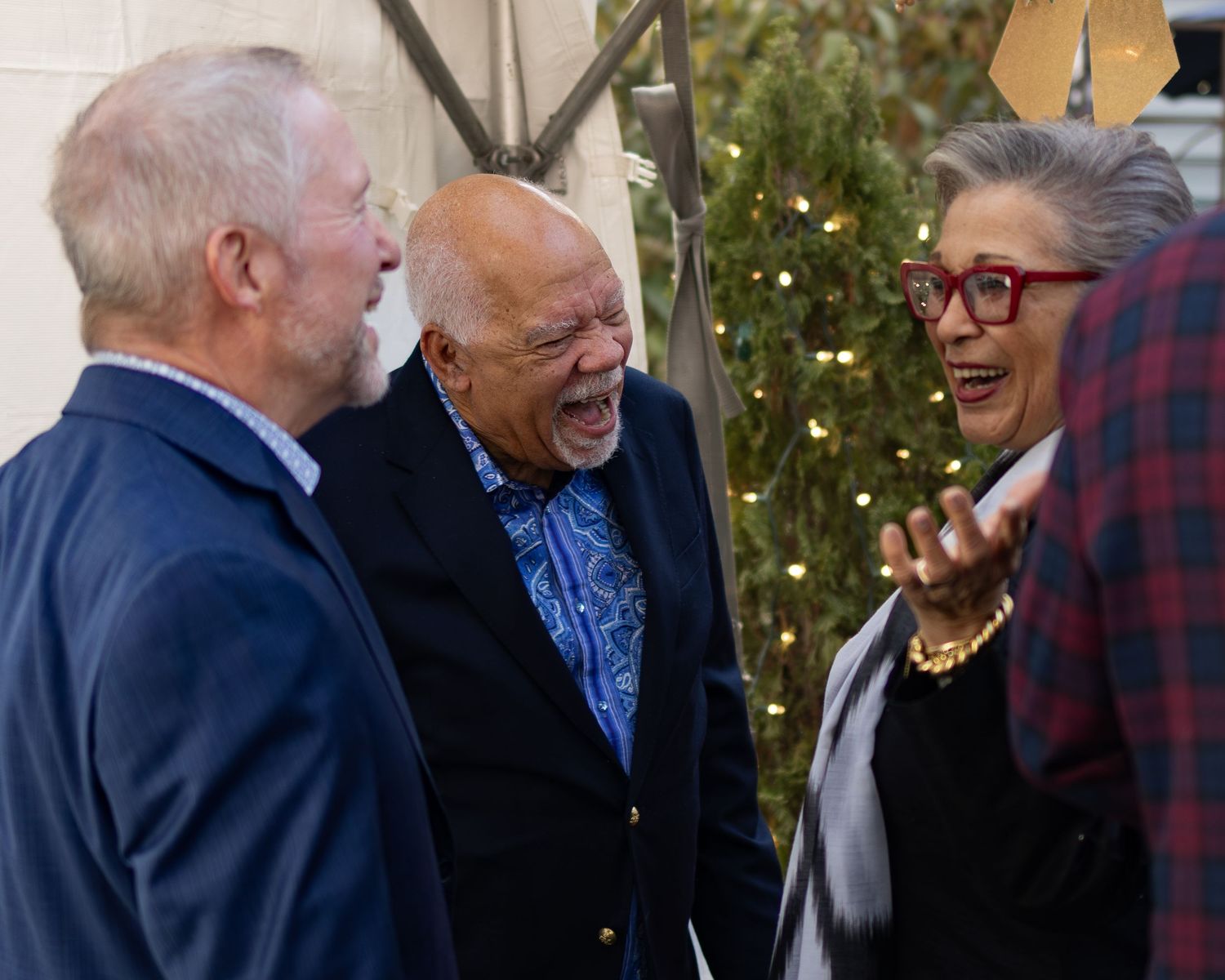 A group of elderly people laughing and socializing together outdoors during a sunny day.