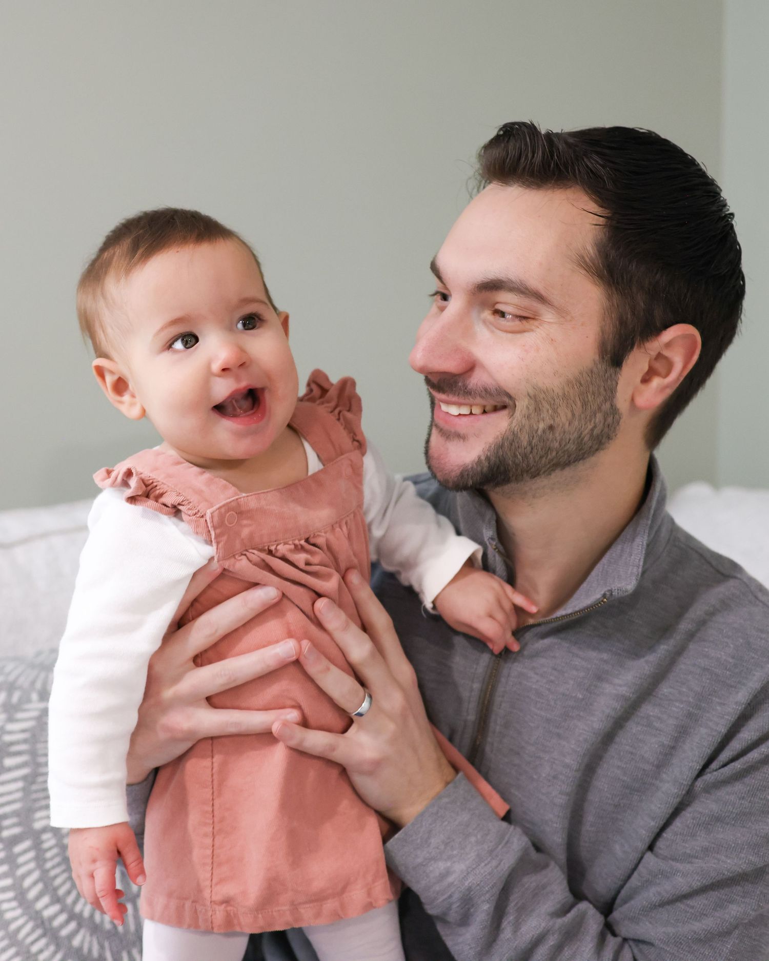 A parent and baby share a tender moment of laughter and cuddles while wearing matching gray and coral outfits.