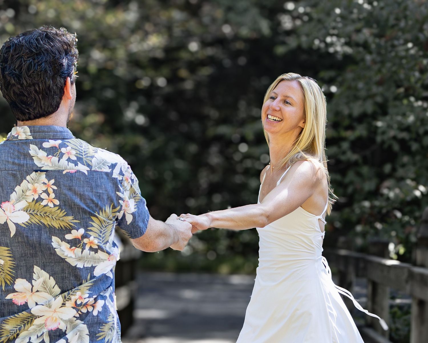A couple in formal wedding attire dances and twirls together in an outdoor garden setting.