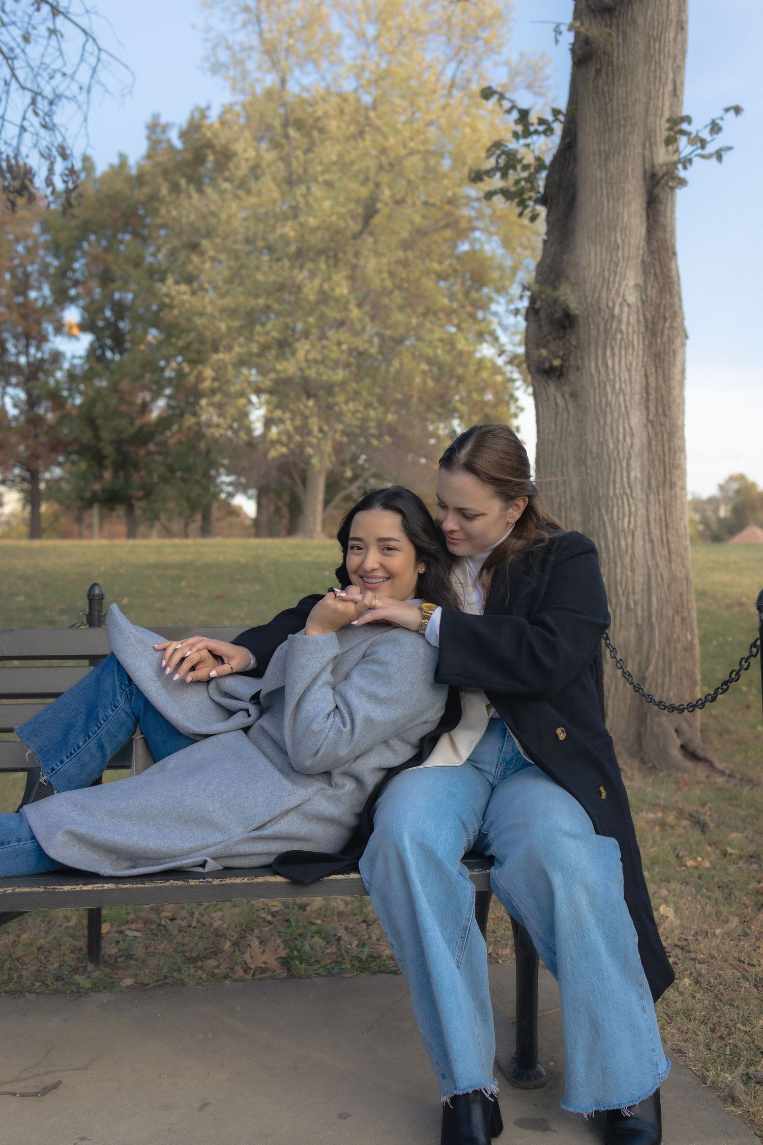 Two friends share a playful moment while relaxing together on a park bench on an autumn afternoon.