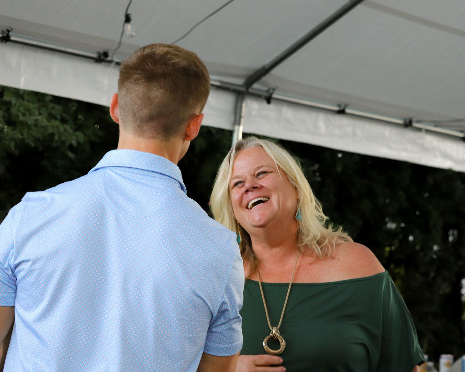 Two people share a candid moment laughing together under a white tent at an outdoor event.