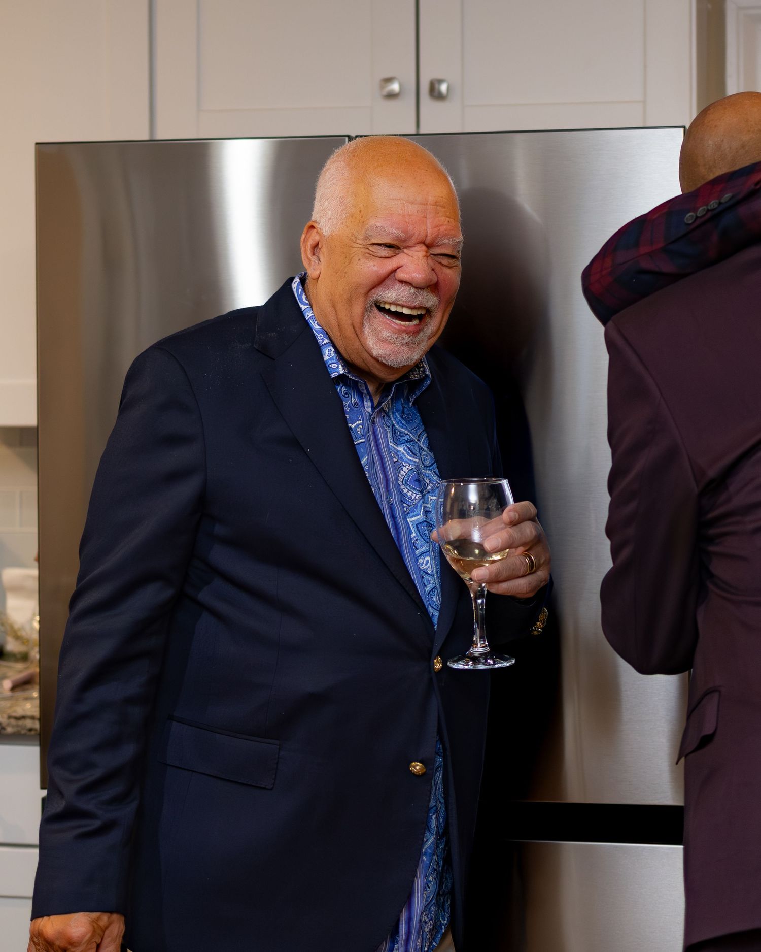 Two men in formal attire share laughter and conversation in an indoor setting.