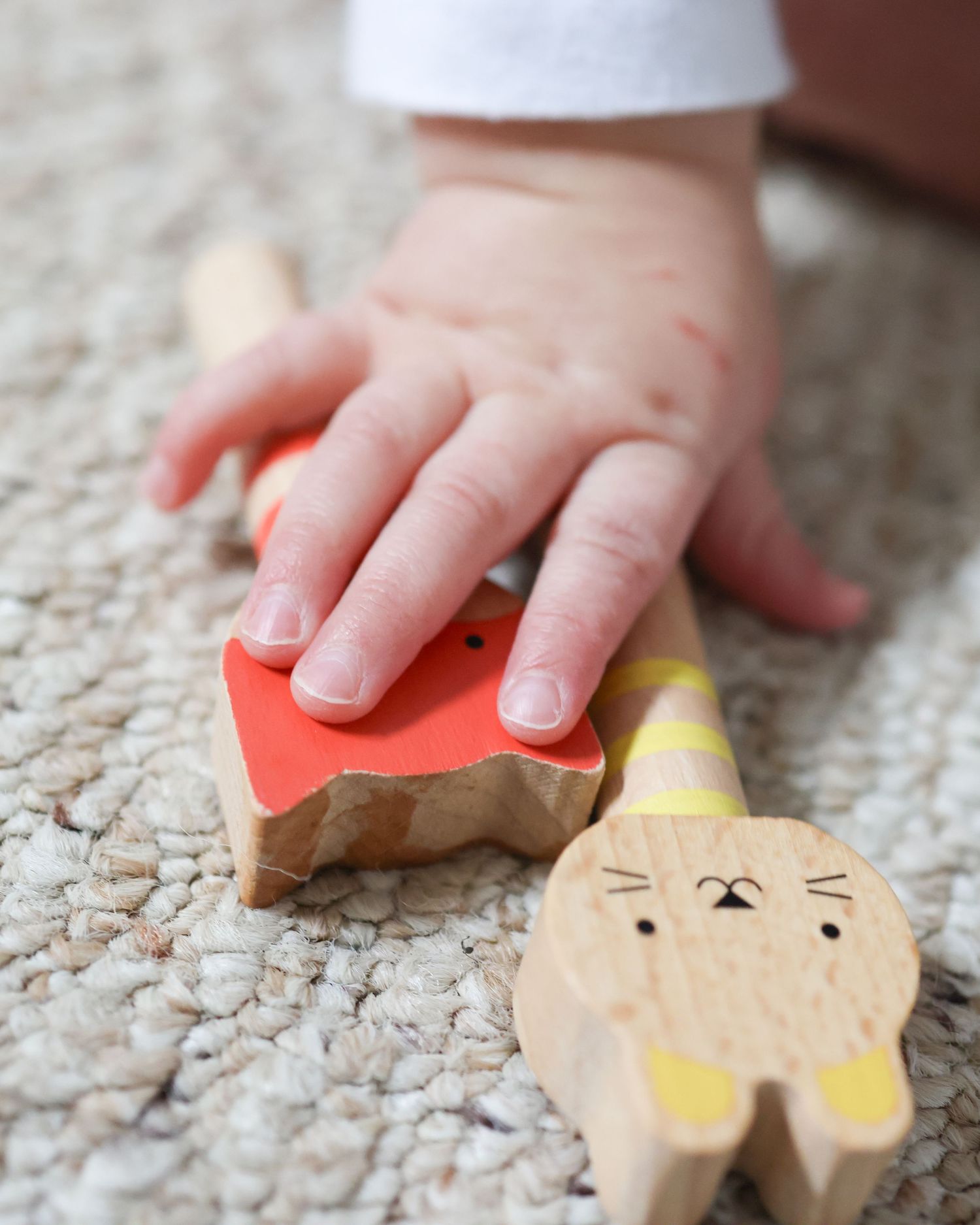 Baby hand reaching for a wooden toy rabbit on a woven rug, colorful painted wooden animal toys for toddlers.