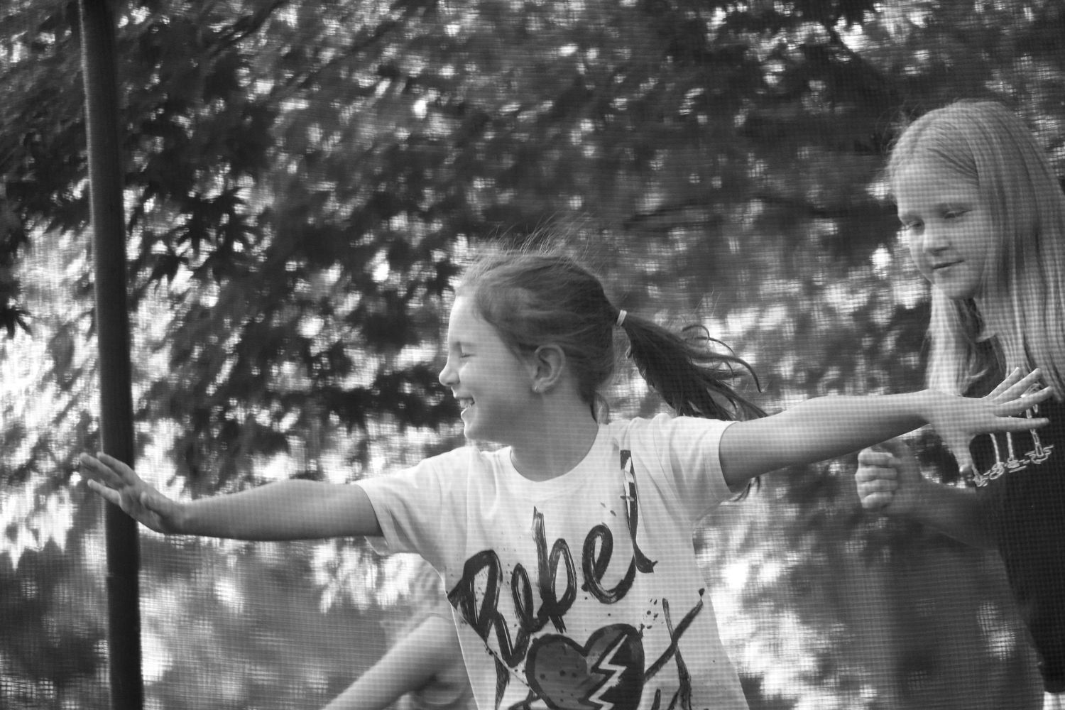 Children play follow the leader in a line outdoors, stretching their arms out wide while walking through a park.