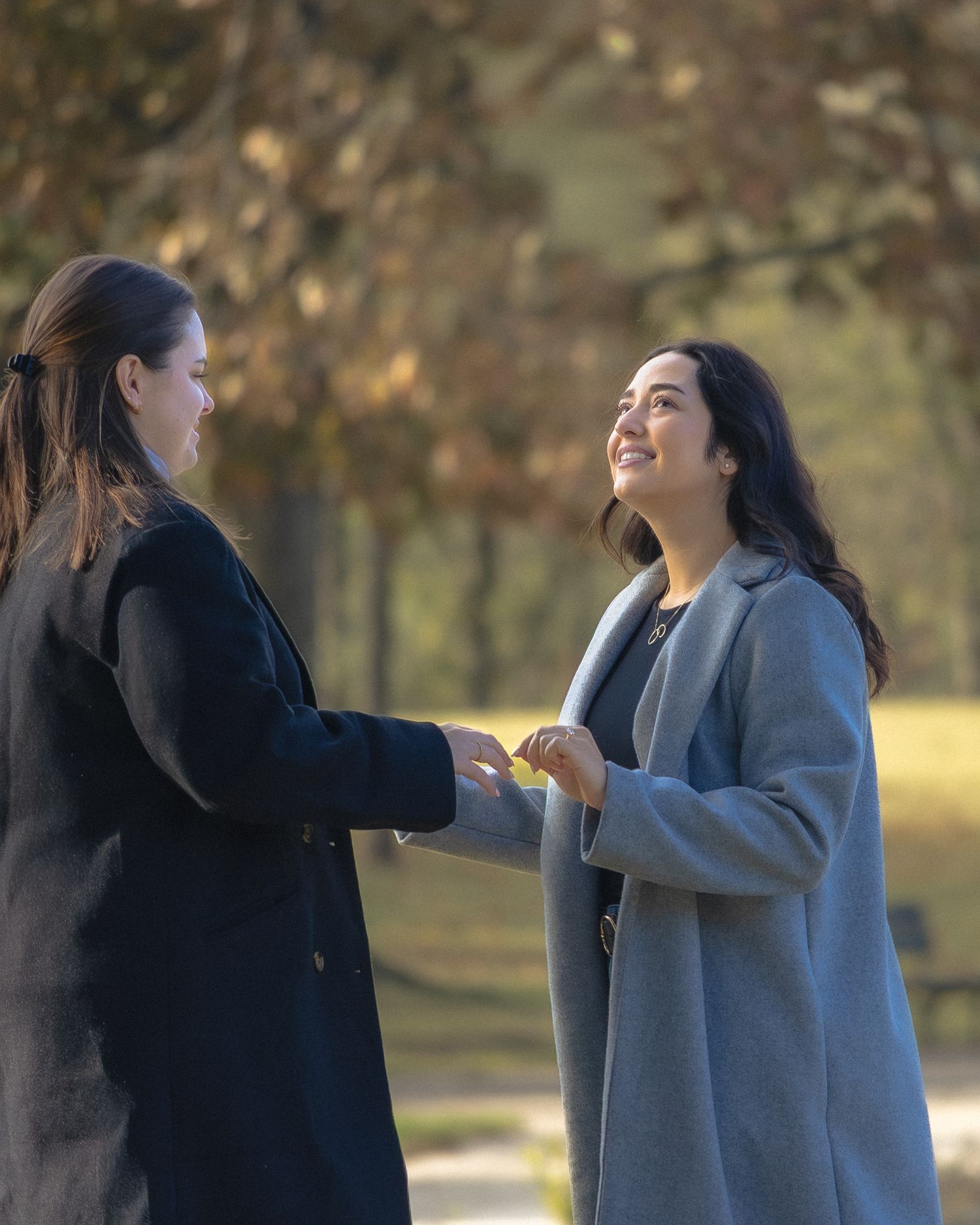 Two people in a park having an animated conversation, one wearing a black coat and one in a gray coat.