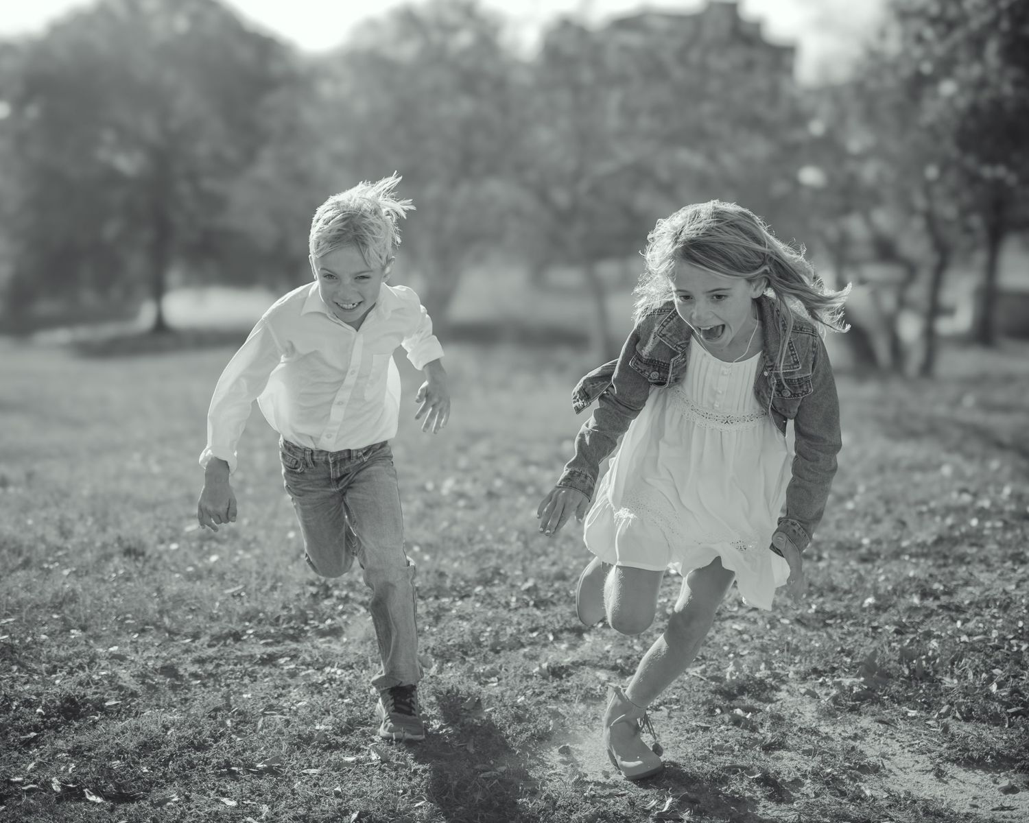 Two children running joyfully through a park in a black and white photo.