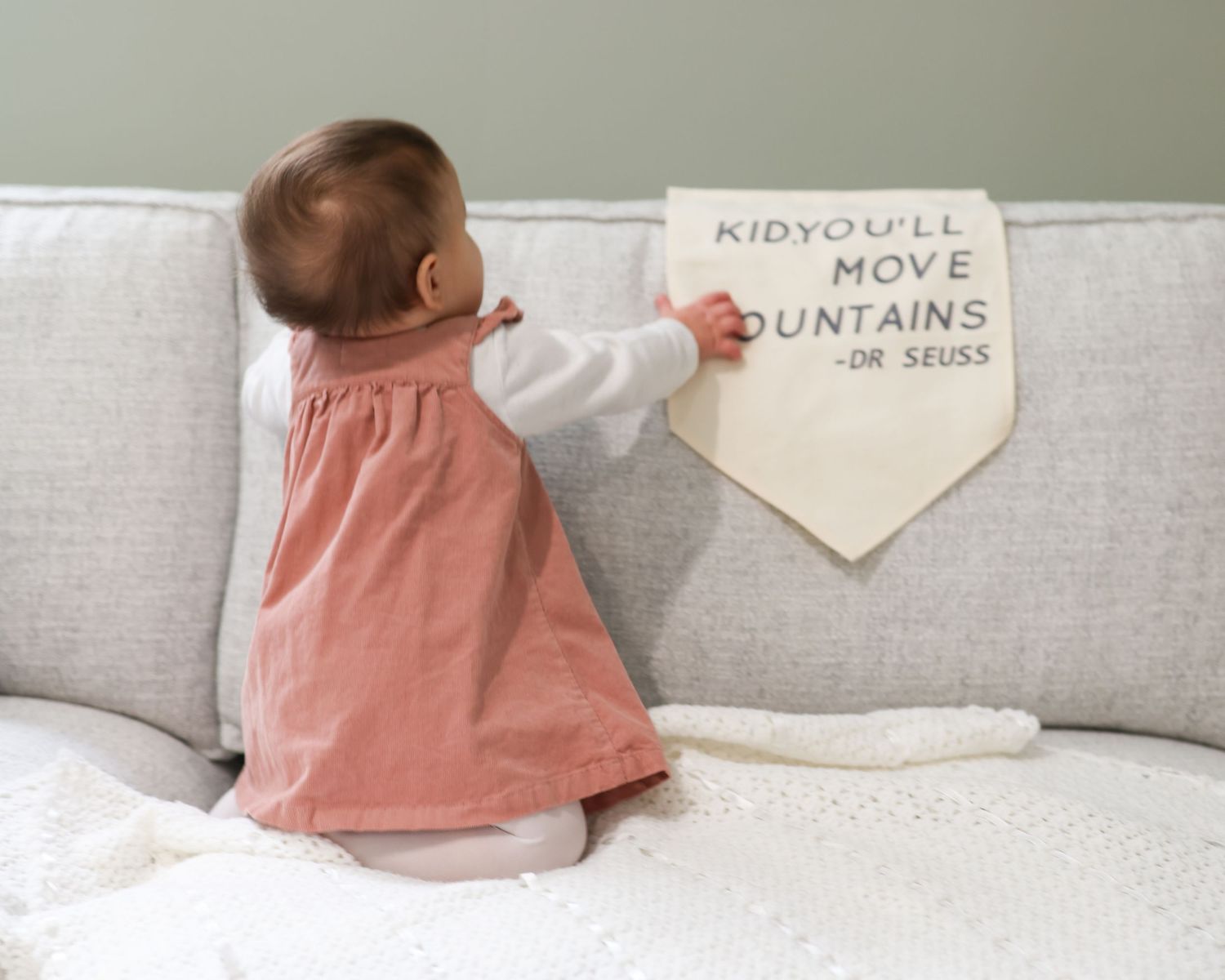 Baby in pink dress reaching toward a canvas banner on a couch with Dr. Seuss quote \