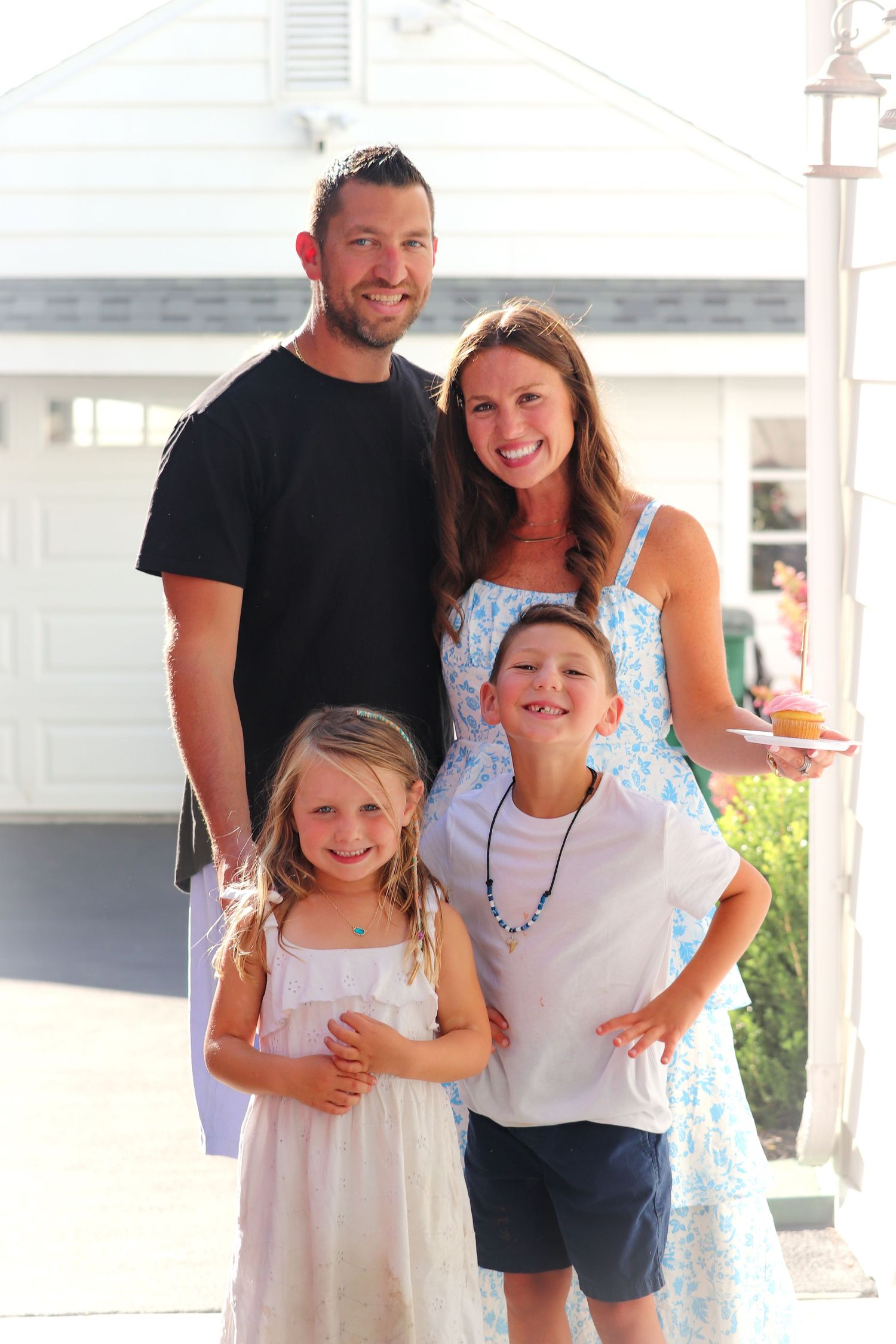 A family poses together outdoors on a sunny day, wearing casual summer attire.