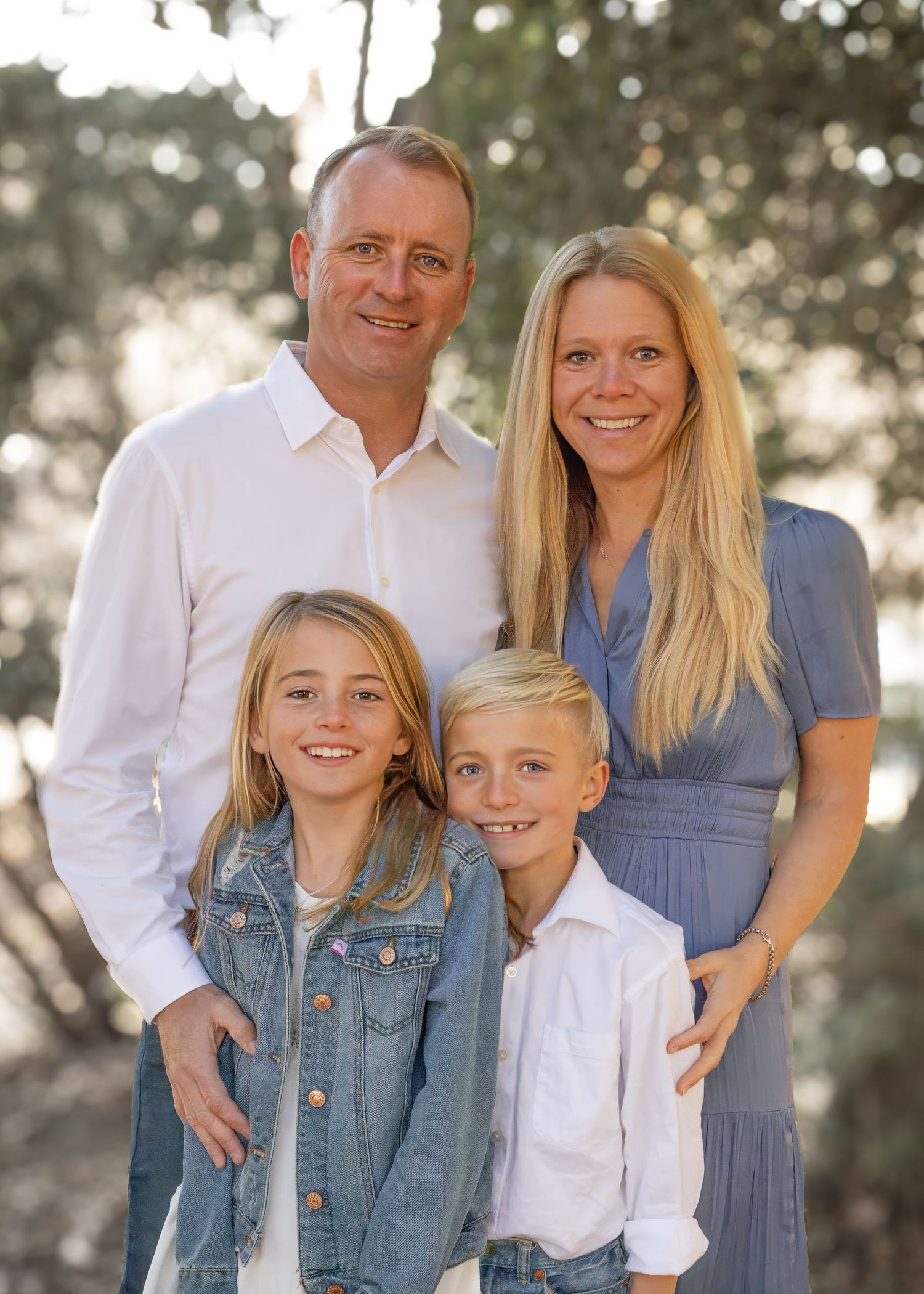 A family wearing coordinated blue and white outfits poses together outdoors during a golden hour photo session.