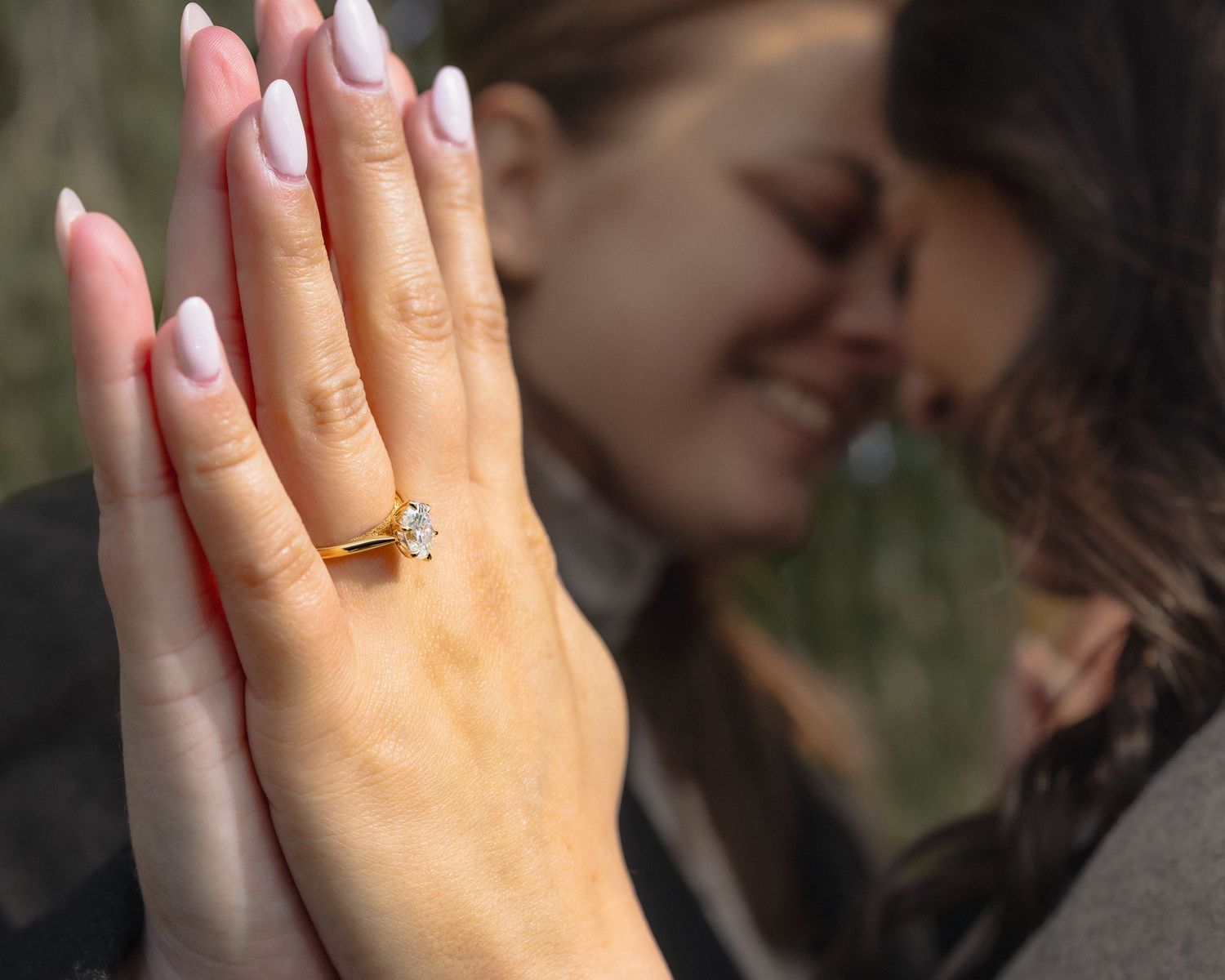Close up shots of hands showing off a sparkling engagement ring against a blurred background.