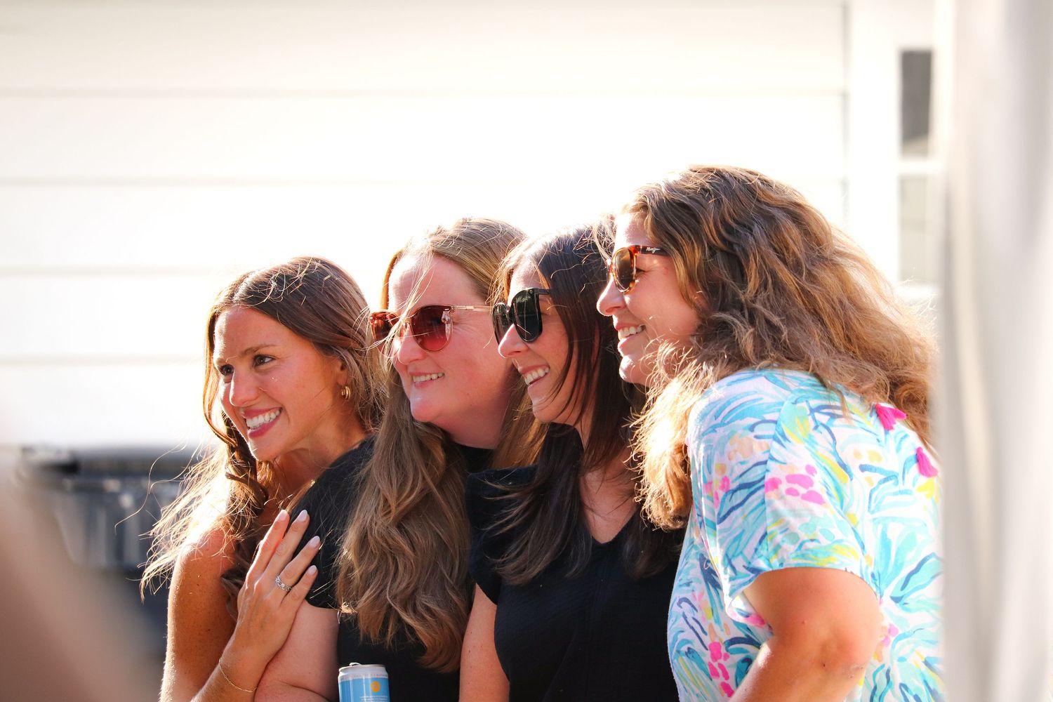 A group of women sitting together in a row and leaning in close while laughing and smiling.